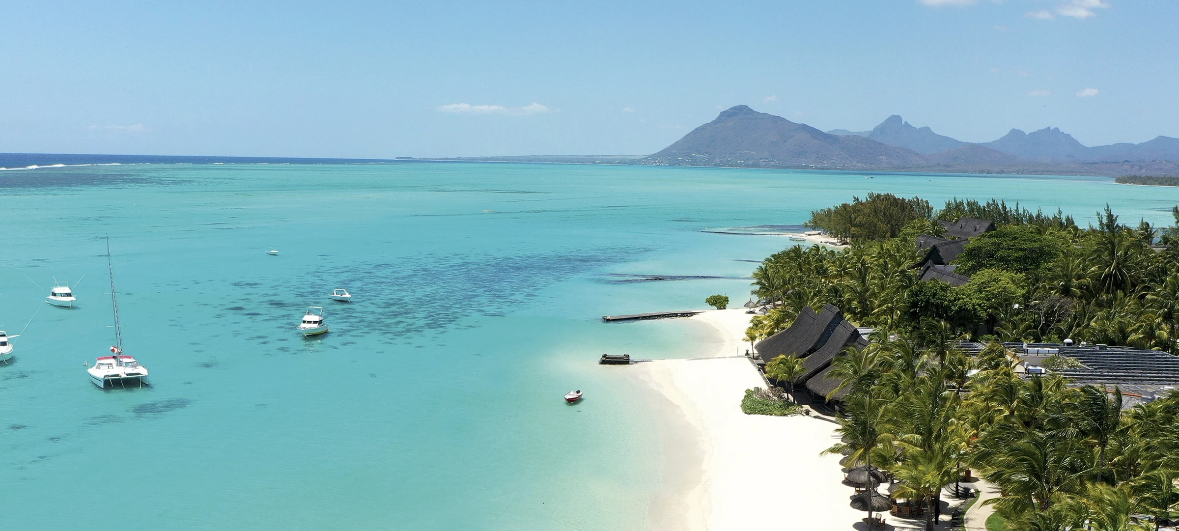 Tropical lagoon in Mauritius with anchored boats, palm-fringed beach, and mountain backdrop—Island Lilly’s signature blend of serenity, culture, and barefoot luxury