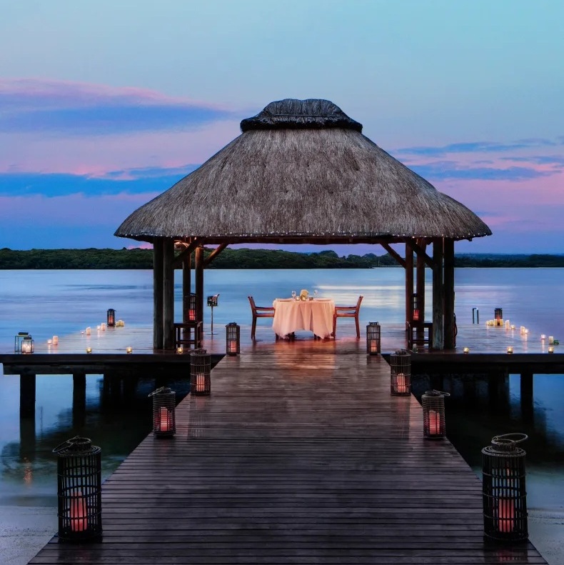 Candlelit dinner table set on a wooden jetty over the lagoon at dusk in Mauritius.