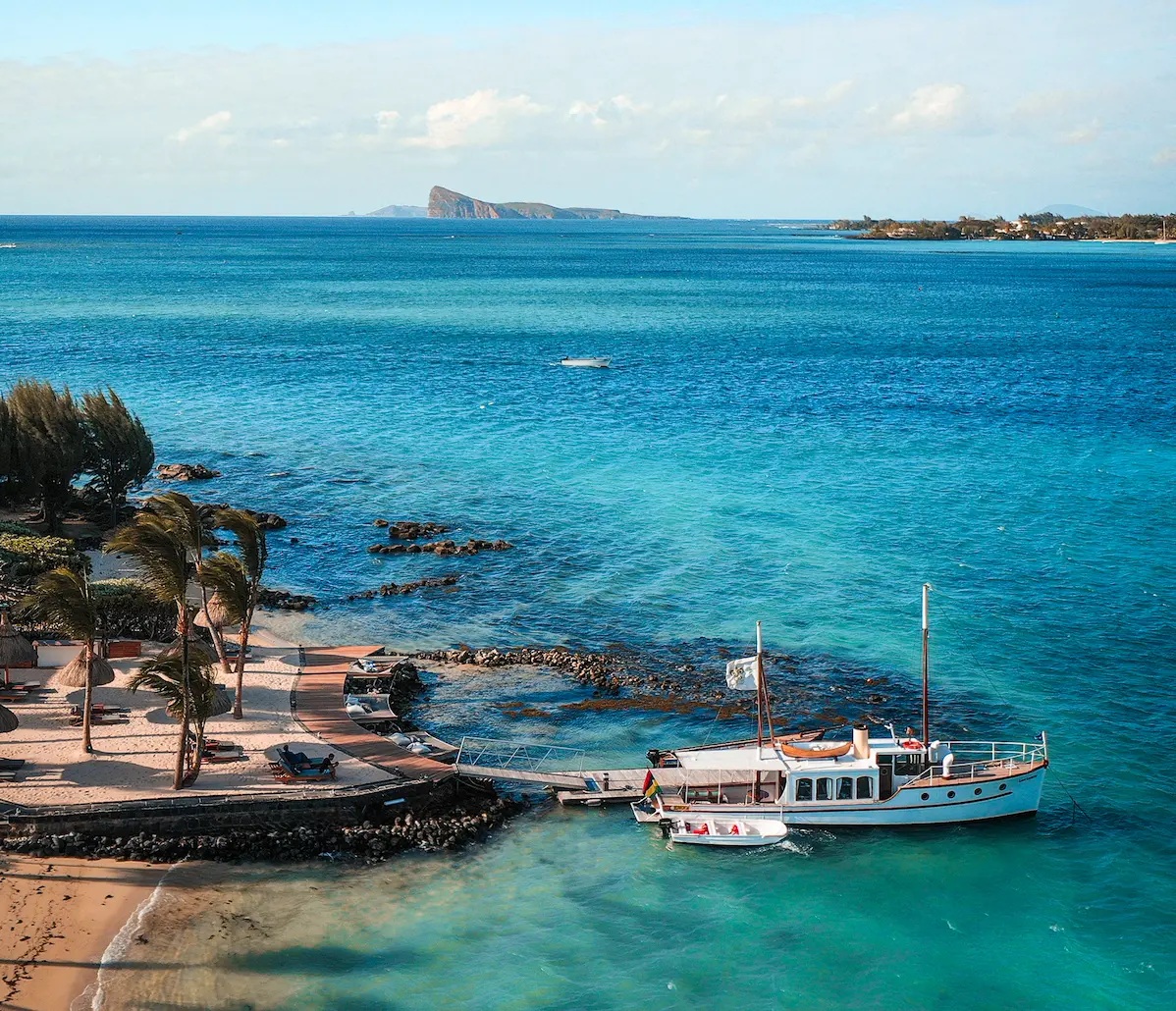 A small boat moored in a turquoise Mauritius lagoon, an islet on the horizon.