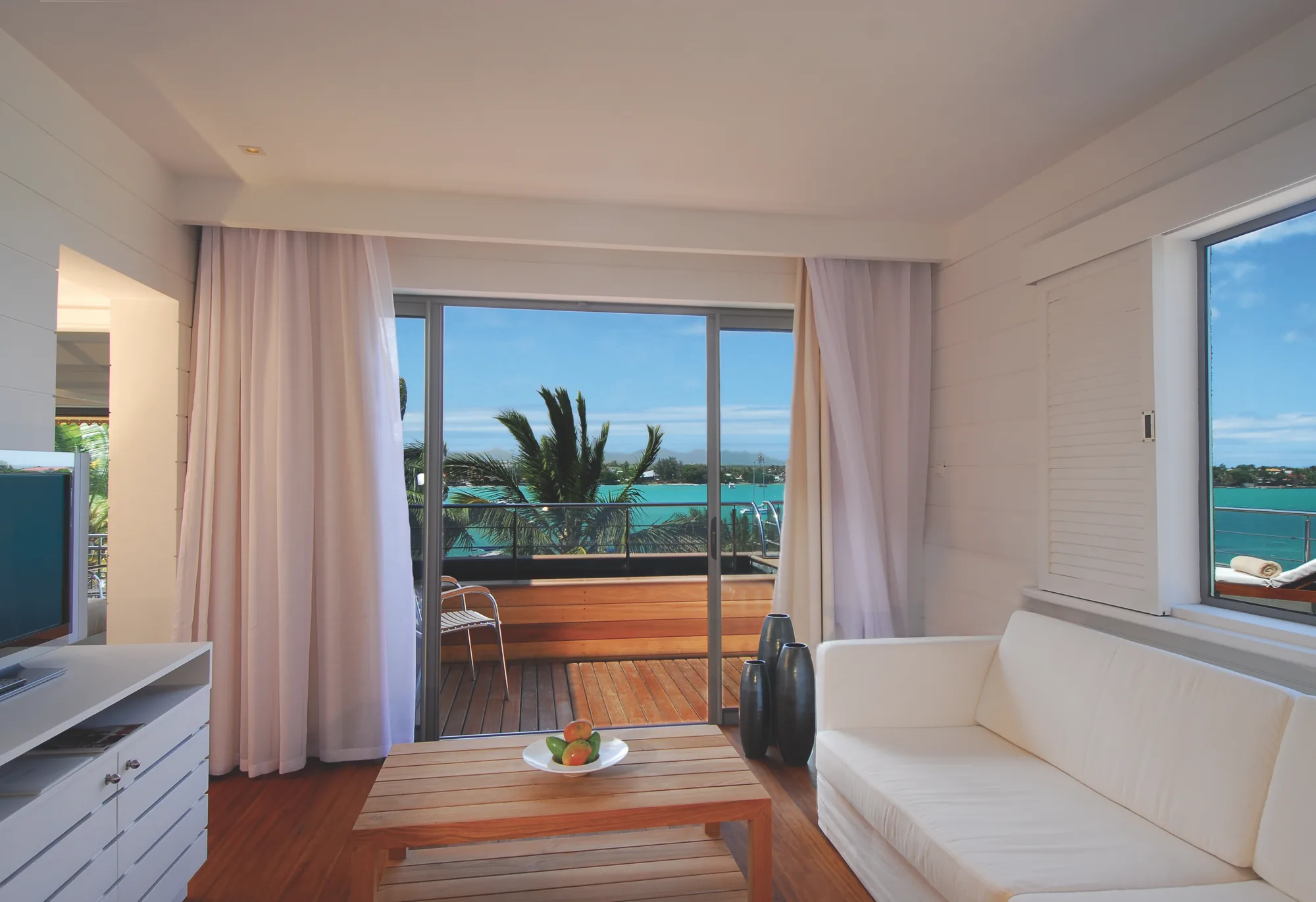 Hotel suite with a wooden floor and green armchair, opening onto a balcony above the sea
