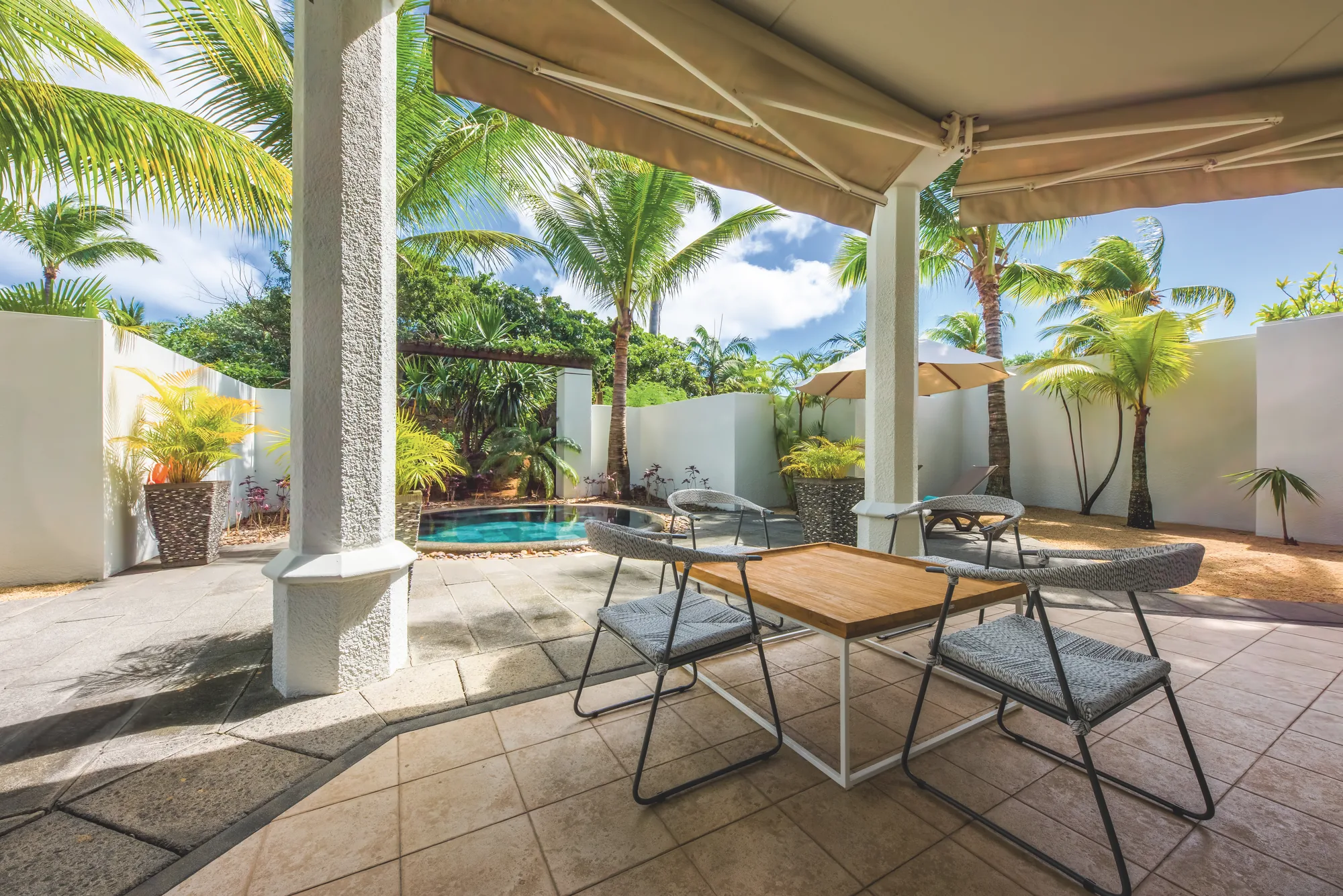 Resort pool with a thatched roof pool bar, cream parasols and loungers, and the lagoon behind