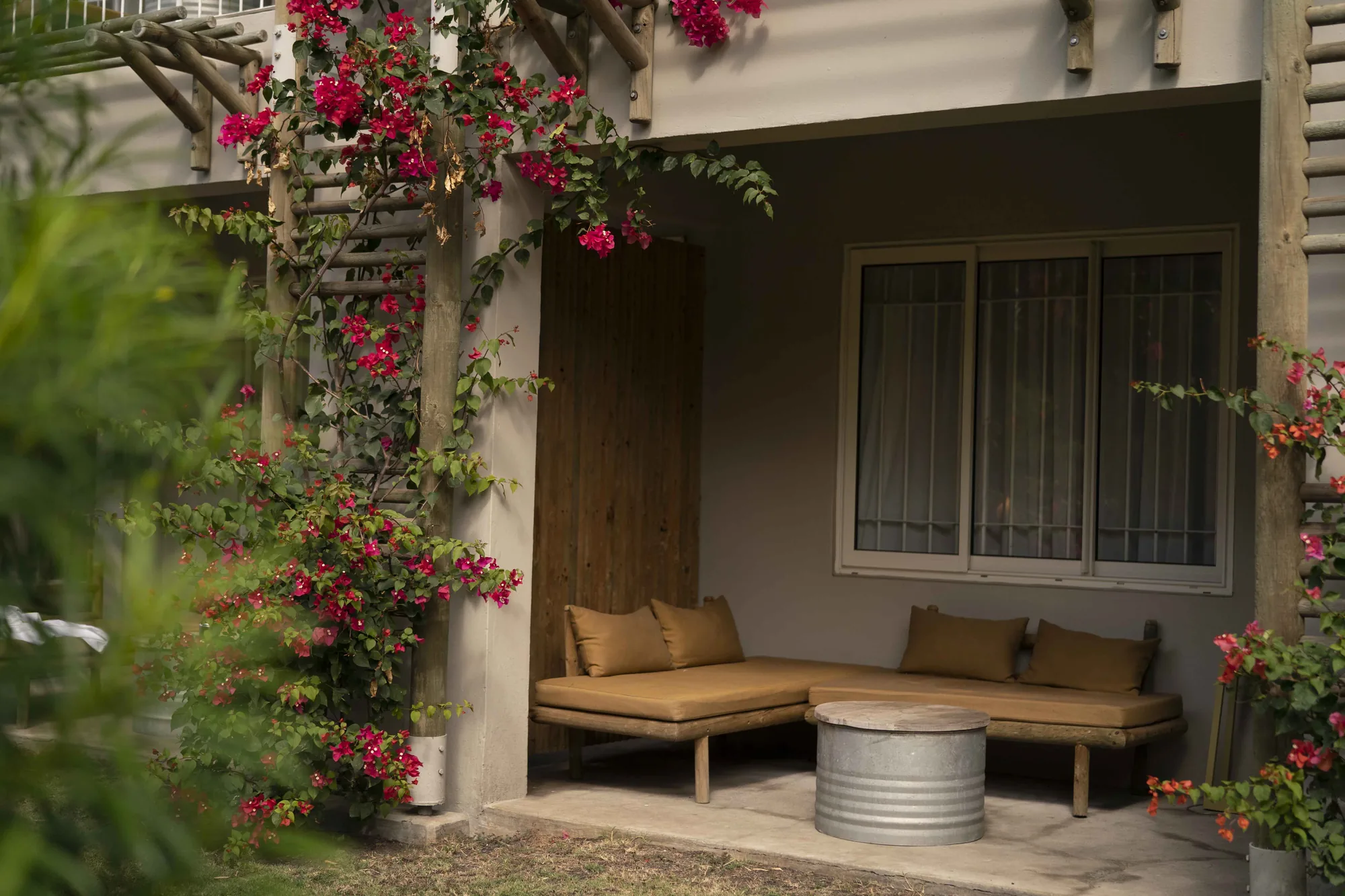 Three guests sitting together on a white cabana daybed under a slatted pergola, palms behind them