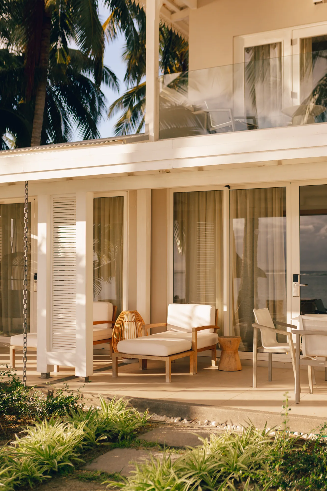Hotel suite with a wooden floor and green armchair, opening onto a balcony above the sea