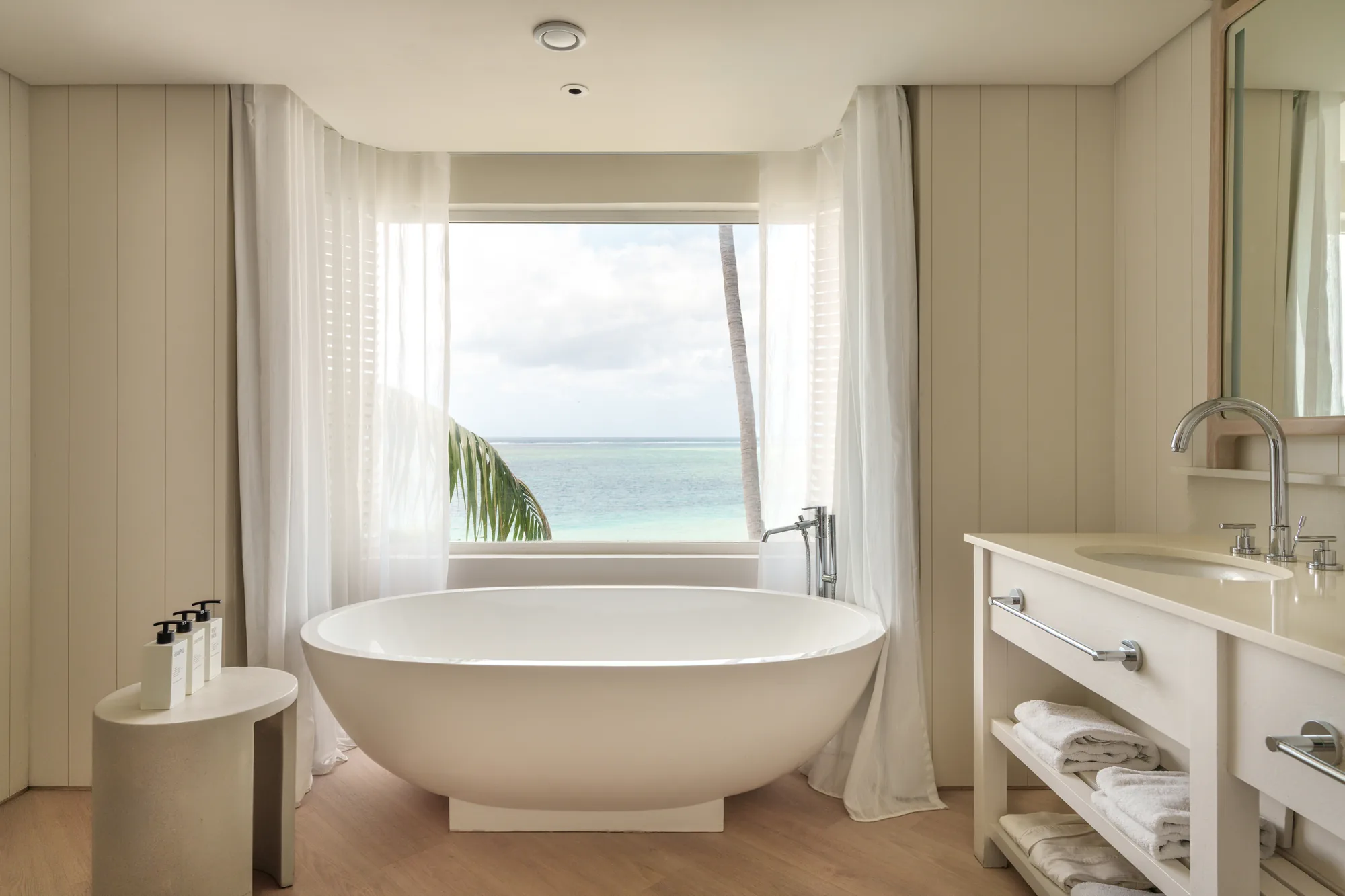 Hotel suite with a wooden floor and green armchair, opening onto a balcony above the sea