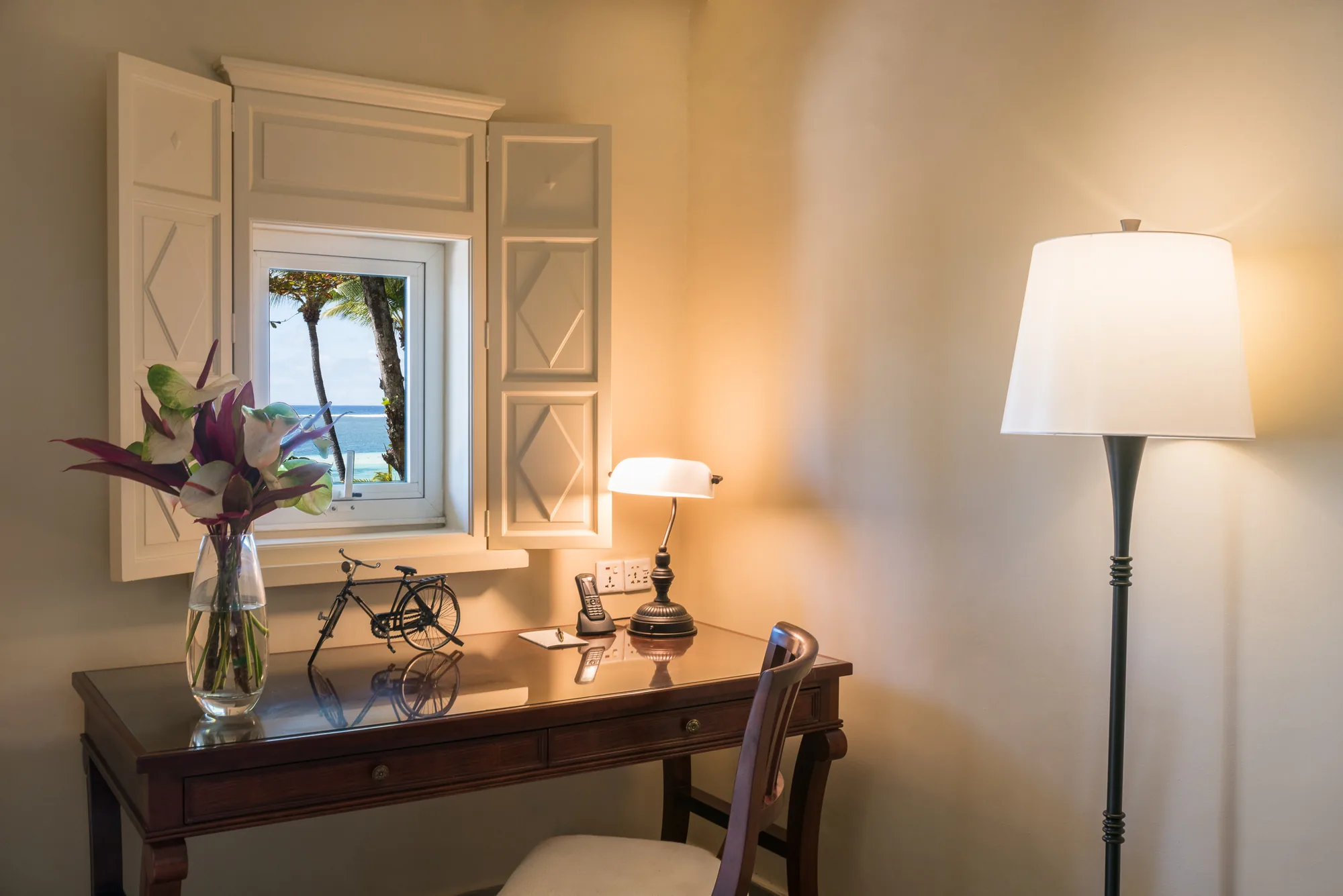 Hotel suite with a wooden floor and green armchair, opening onto a balcony above the sea