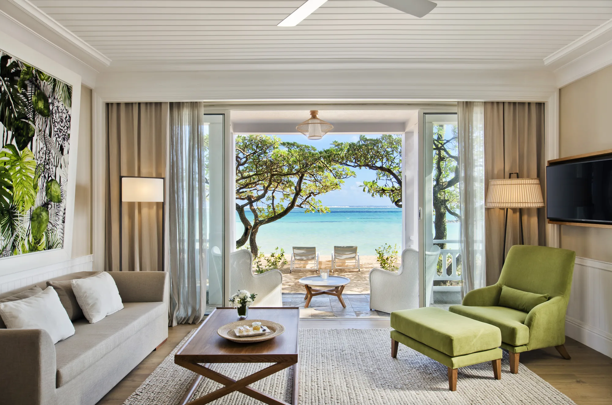 Hotel suite with a wooden floor and green armchair, opening onto a balcony above the sea