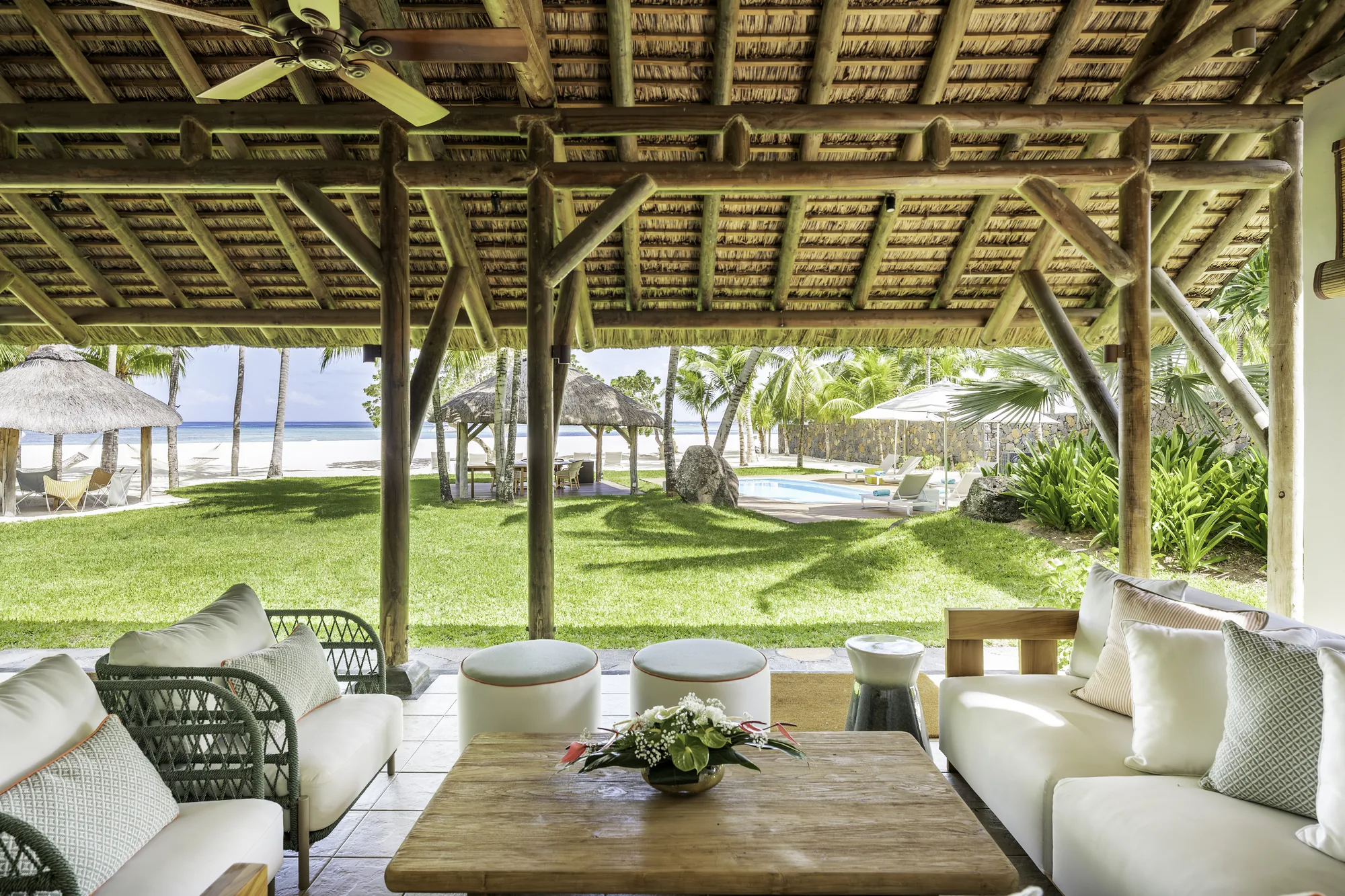 Resort pool with a thatched roof pool bar, cream parasols and loungers, and the lagoon behind
