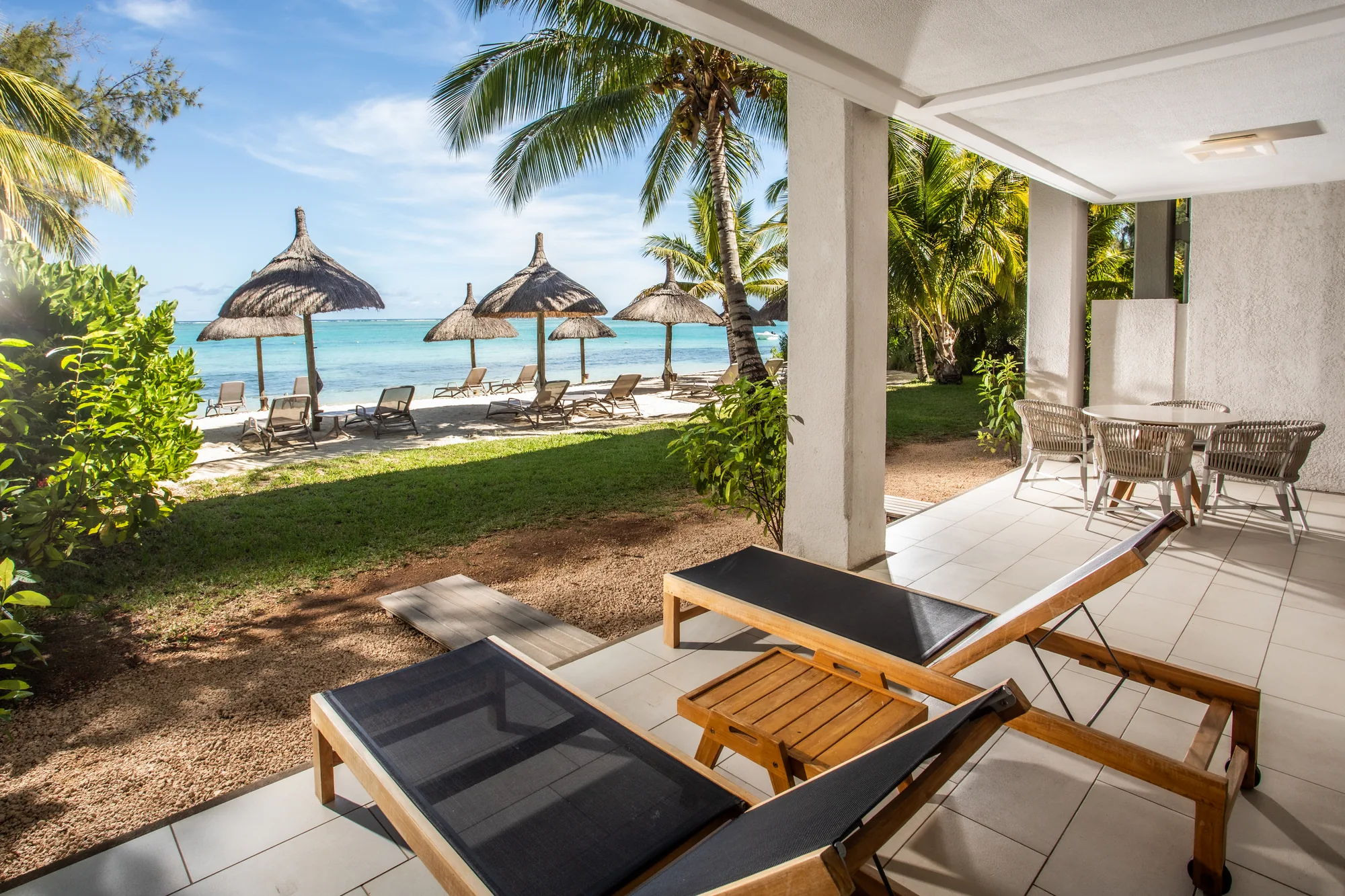 Hotel suite with a wooden floor and green armchair, opening onto a balcony above the sea