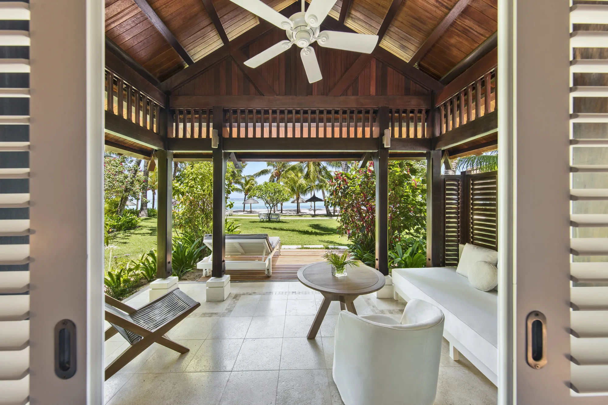 Hotel suite with a wooden floor and green armchair, opening onto a balcony above the sea