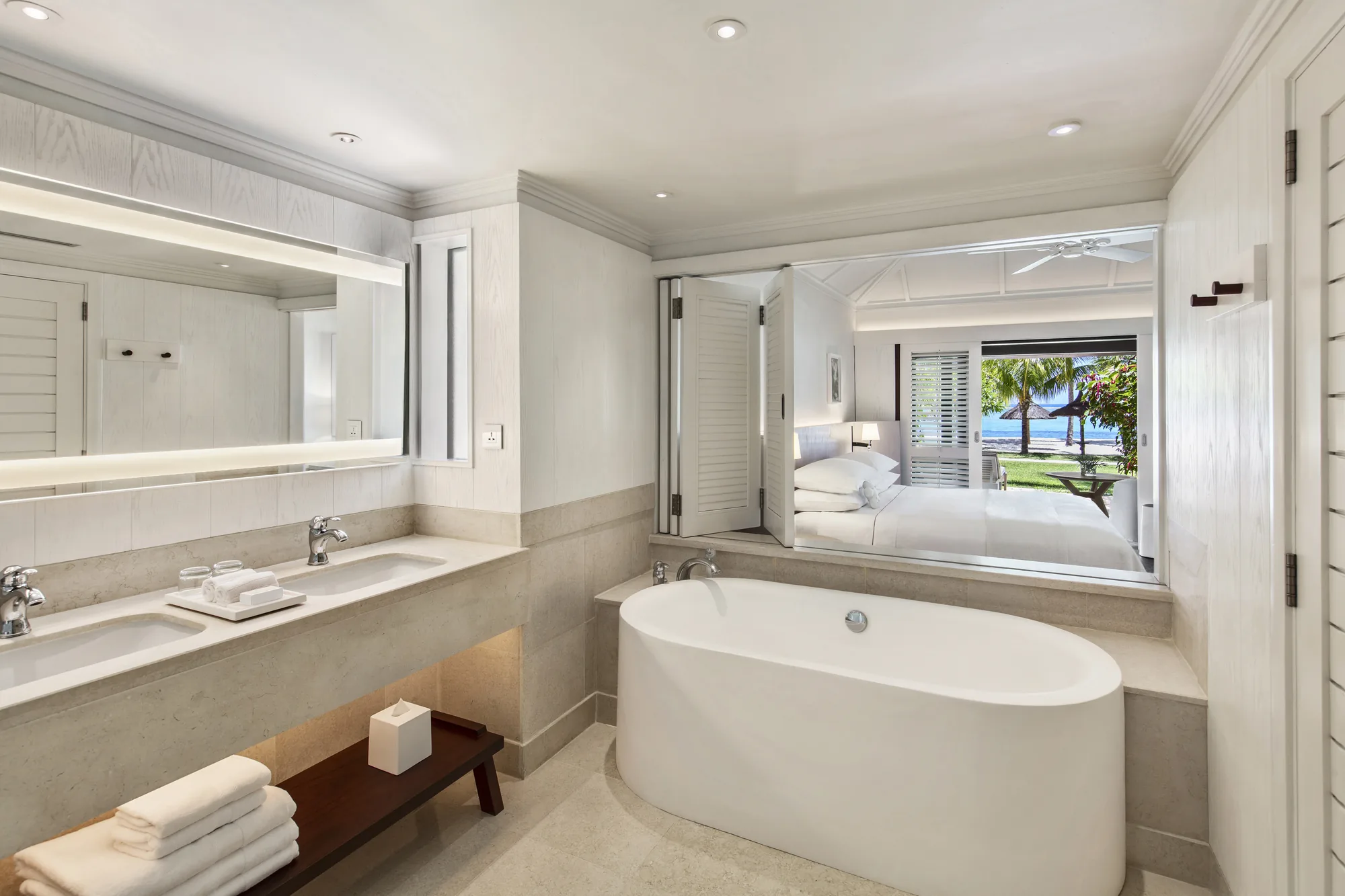 Resort pool with a thatched roof pool bar, cream parasols and loungers, and the lagoon behind