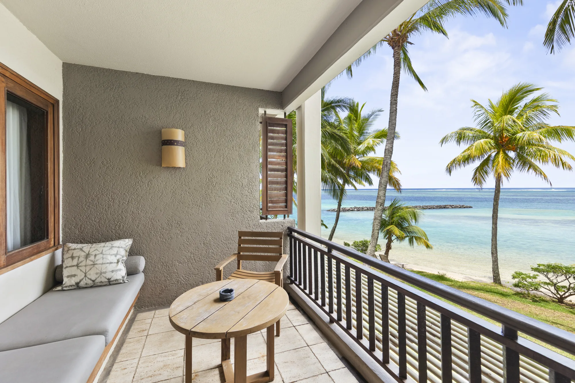 Hotel suite with a wooden floor and green armchair, opening onto a balcony above the sea