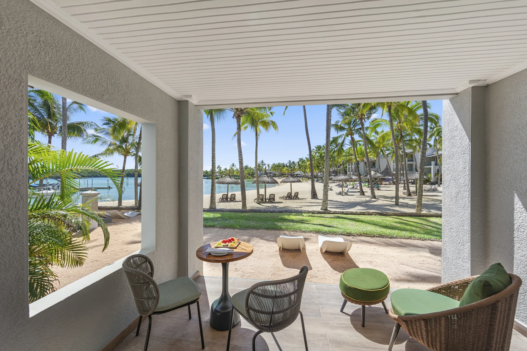 Resort pool with a thatched roof pool bar, cream parasols and loungers, and the lagoon behind