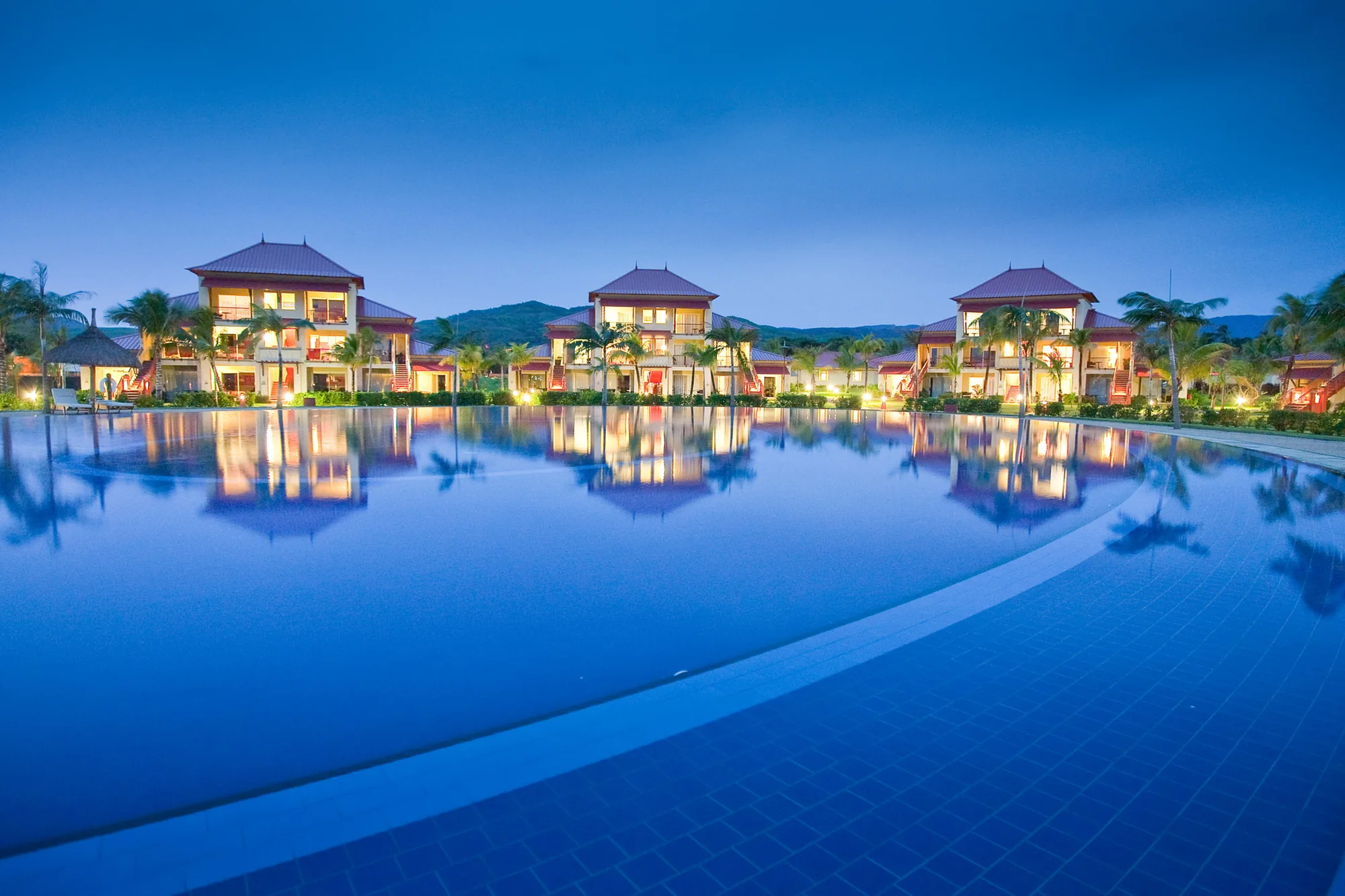 A long pool at dusk, with the lit buildings reflected in the water