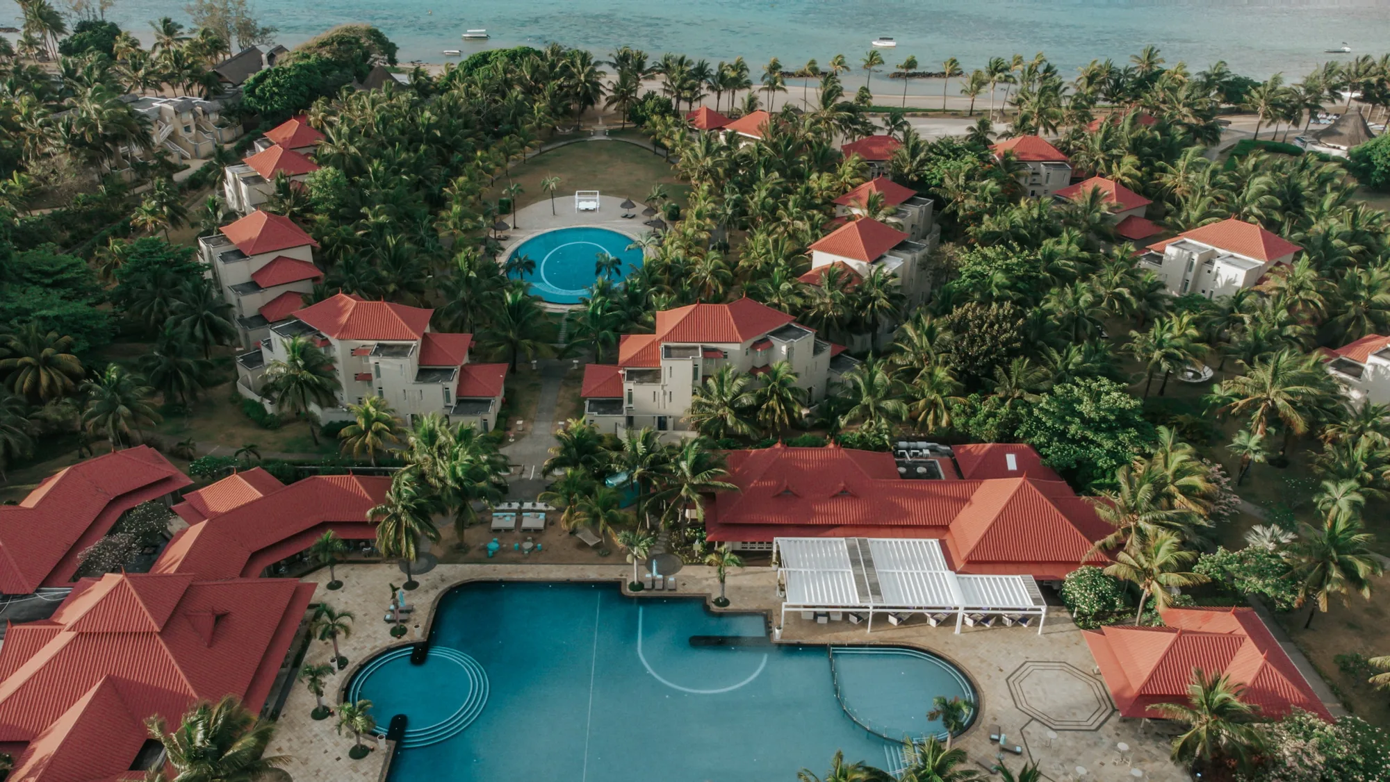 Red-roofed accommodation blocks around a pool and gardens, seen from above