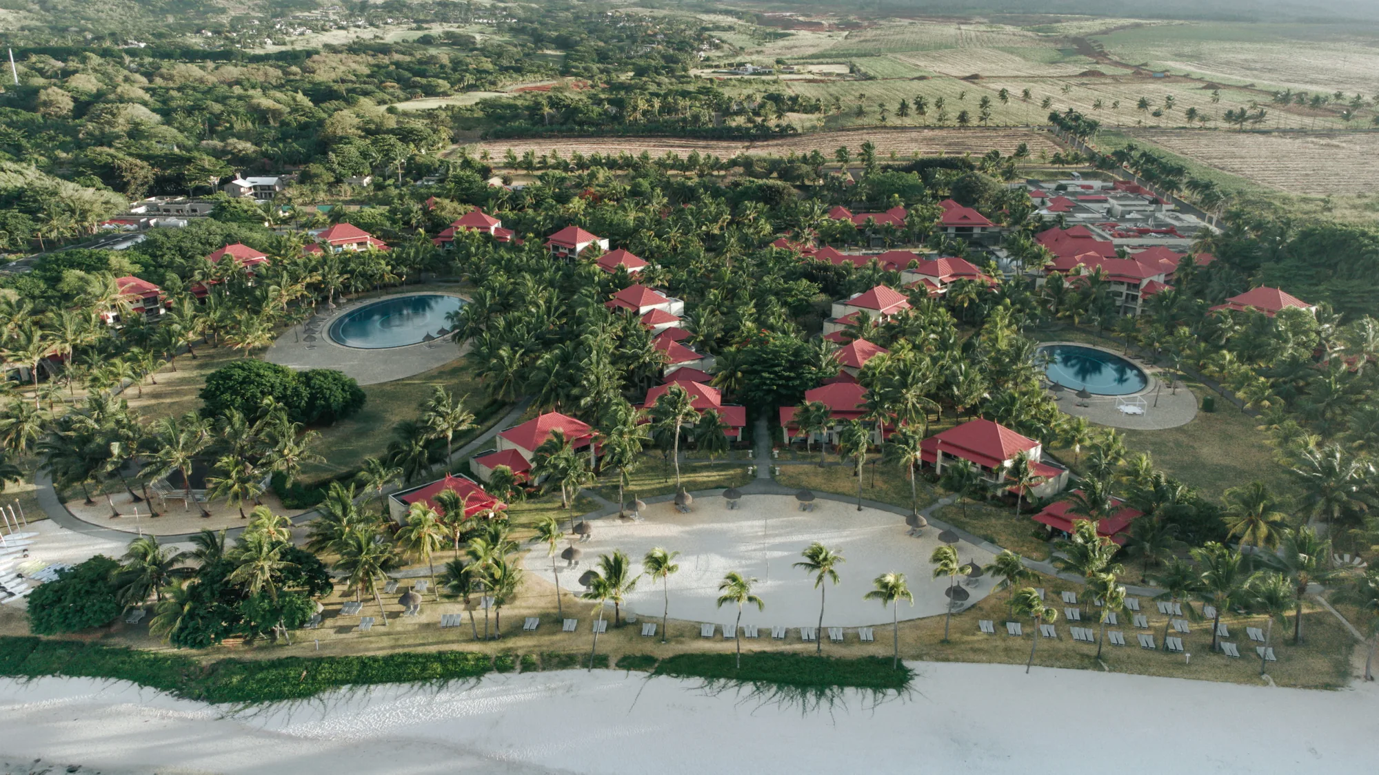 Aerial view of Tamassa Bel Ombre, its red-roofed buildings and pools set among trees behind the beach
