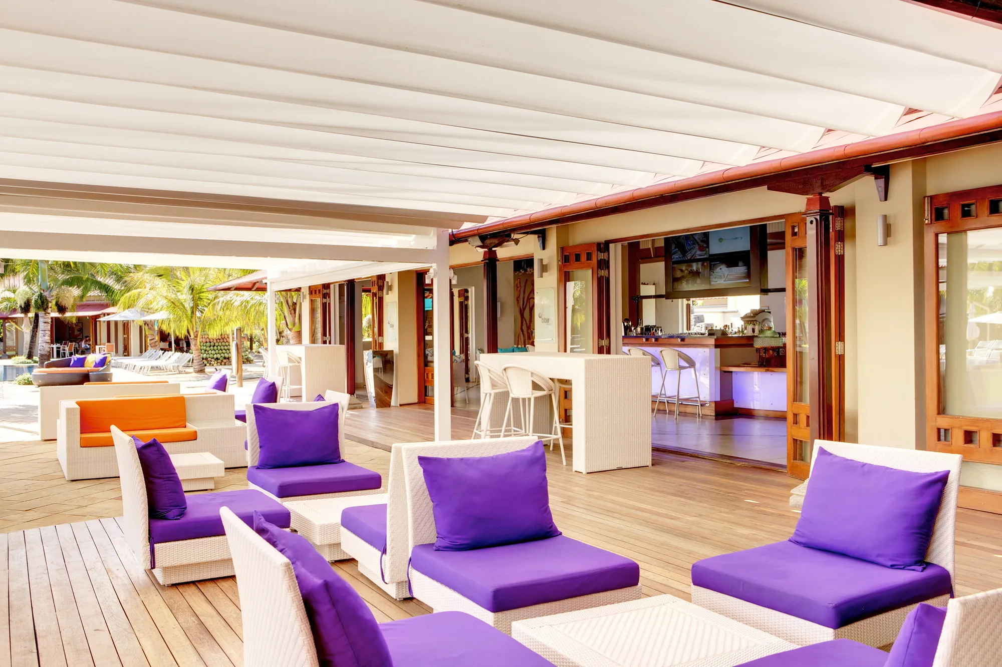 An open-sided lounge with white chairs and purple cushions under a pergola