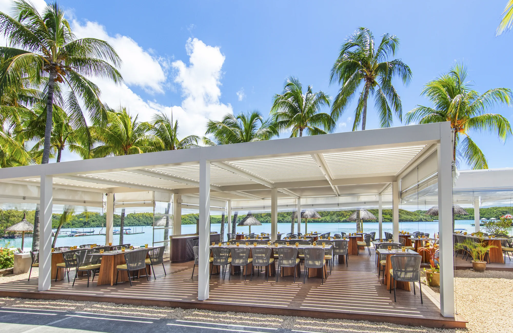 A white pergola restaurant on a deck beside the lagoon