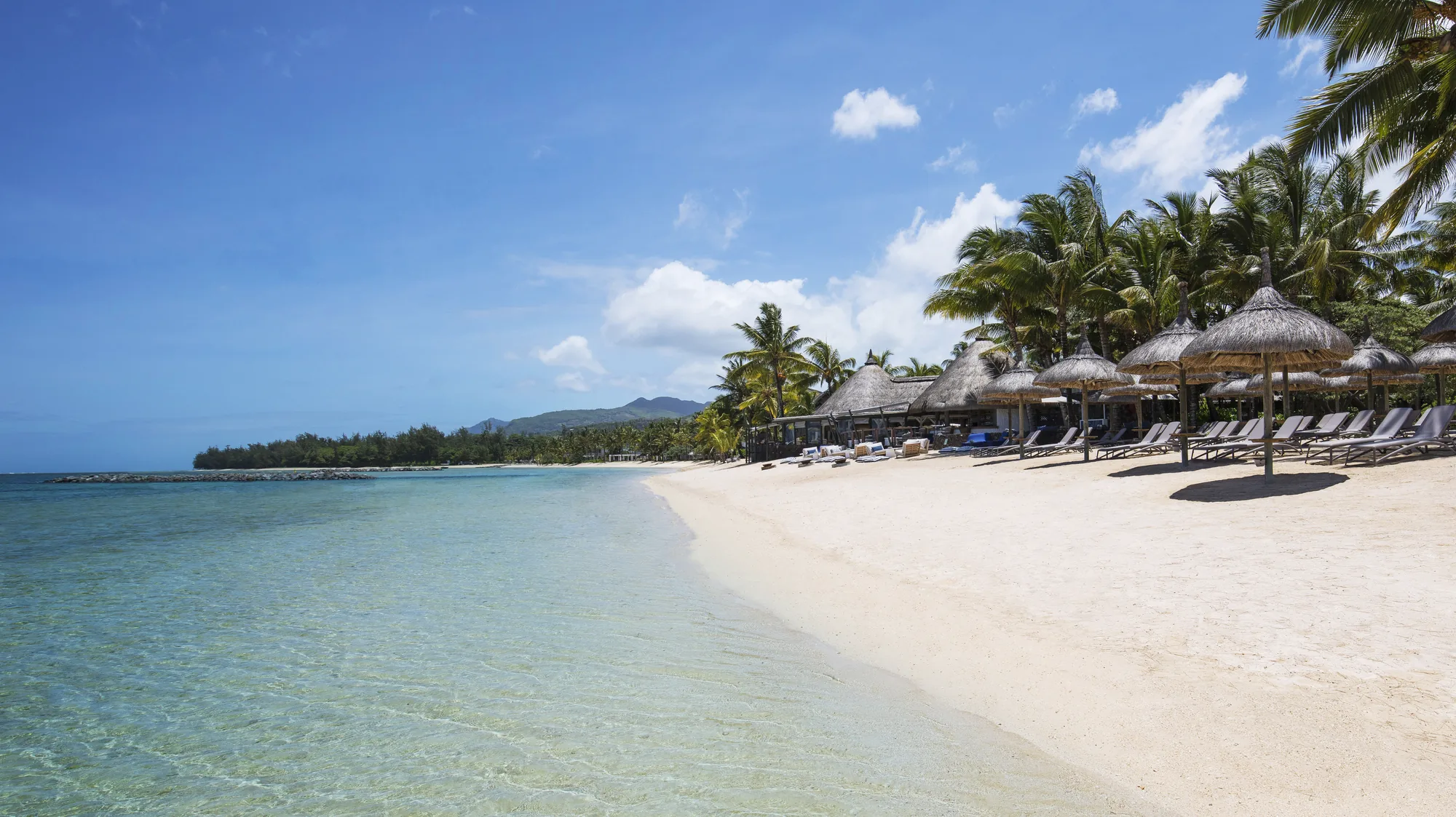 The beach at Heritage Awali Golf & Spa Resort, with thatched parasols along the white sand