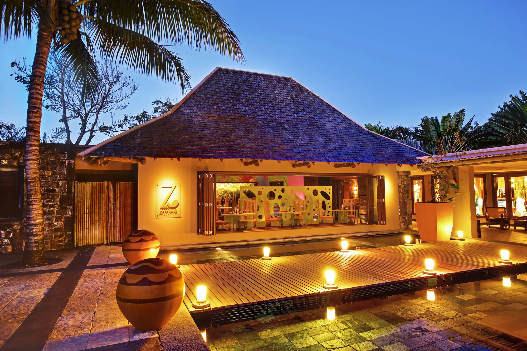 A restaurant entrance lit in the evening, with lanterns along a wooden deck