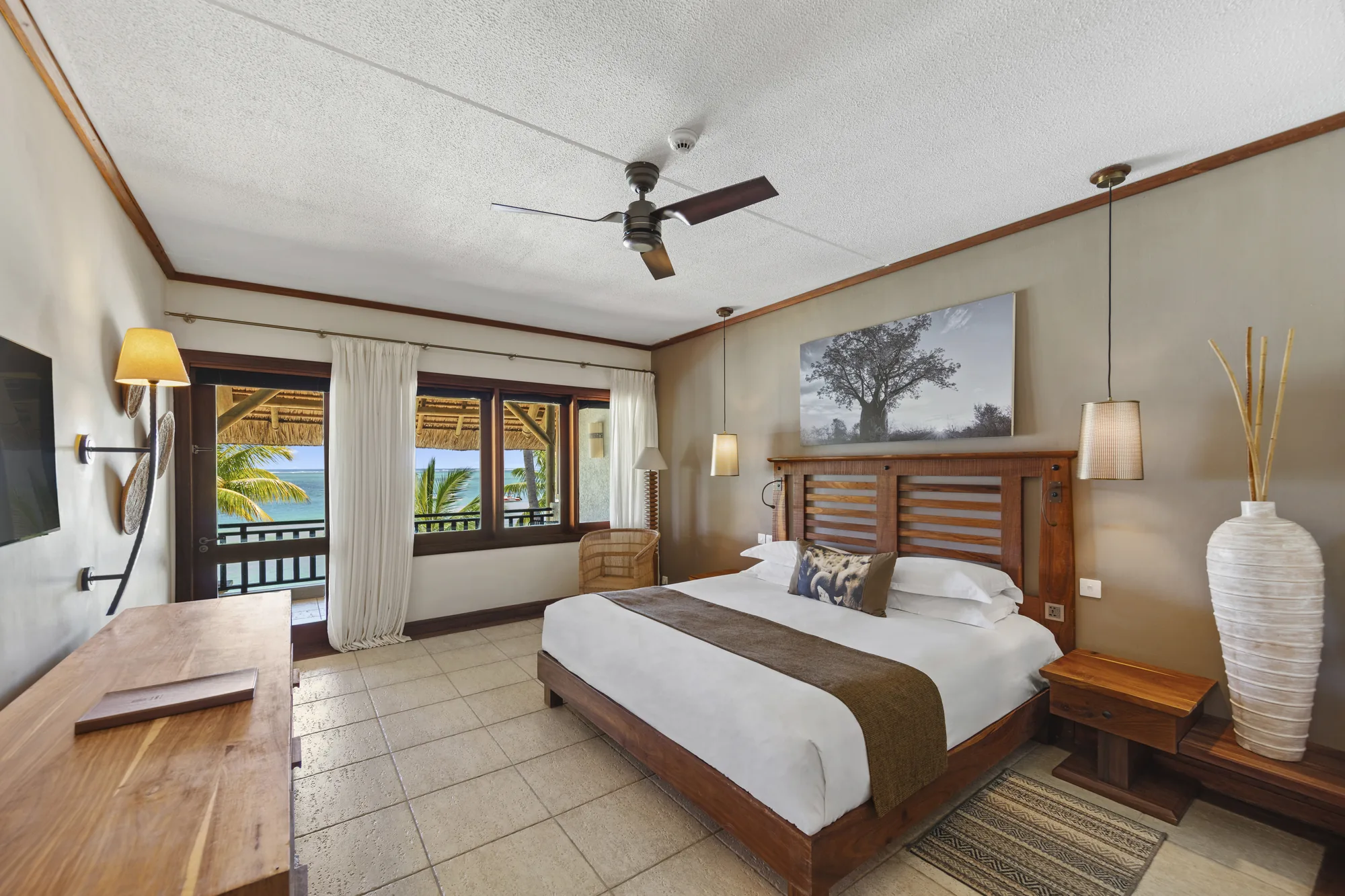 A bedroom with a wooden bed, a ceiling fan and a window onto the balcony
