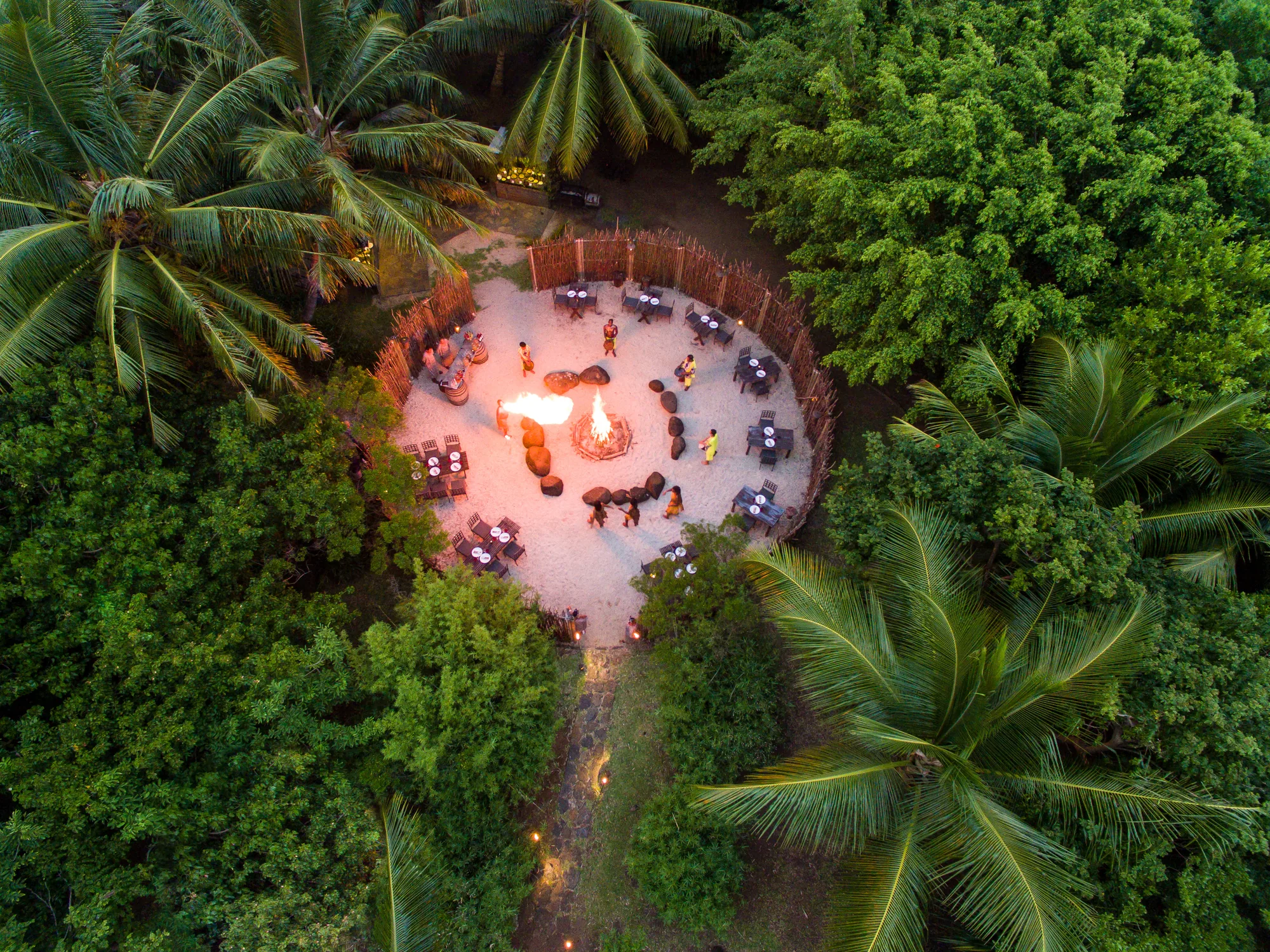 Aerial view of a candlelit dinner set out in a clearing among palm trees