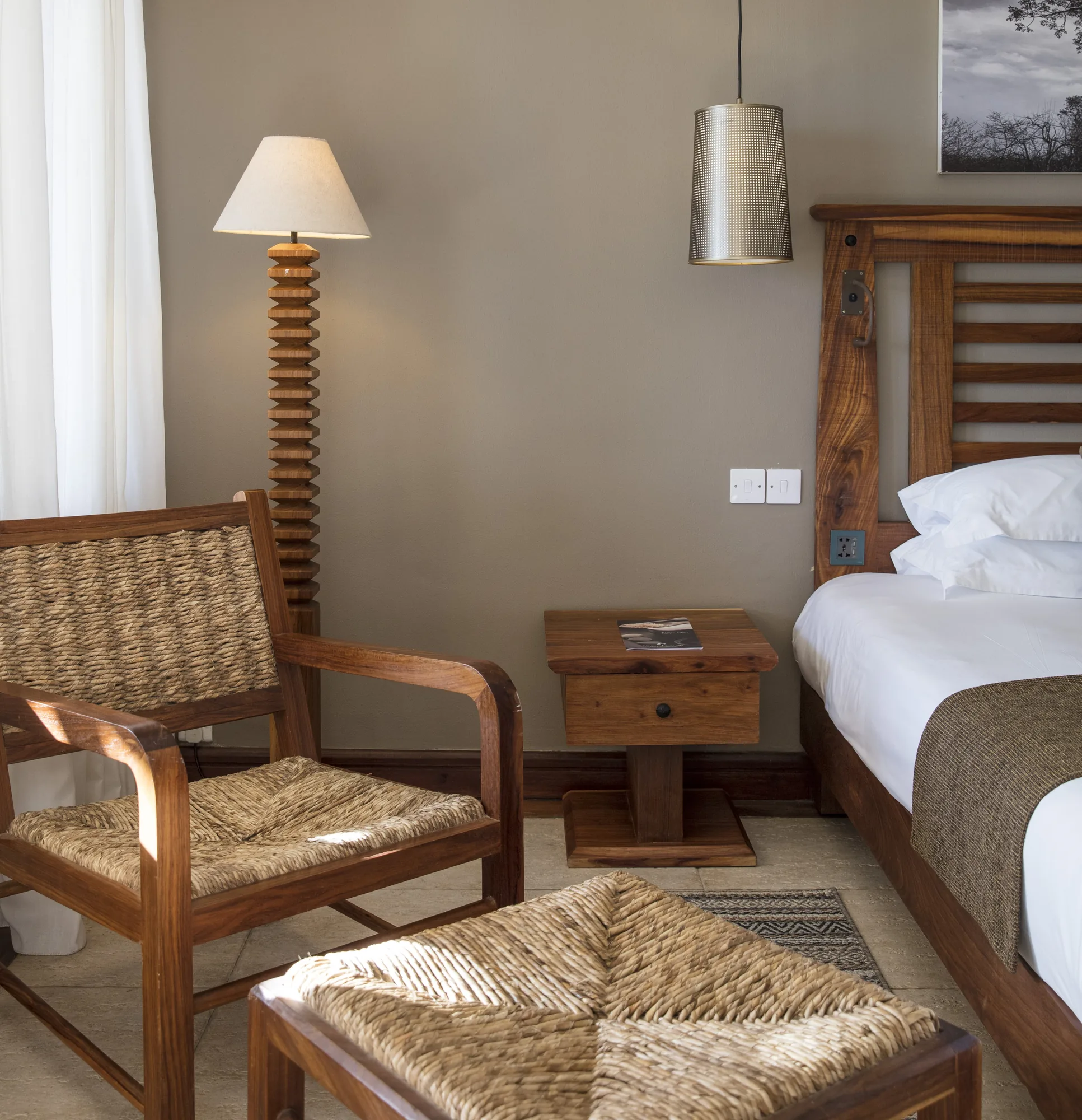 A bedroom corner with a woven armchair, footstool and bedside table