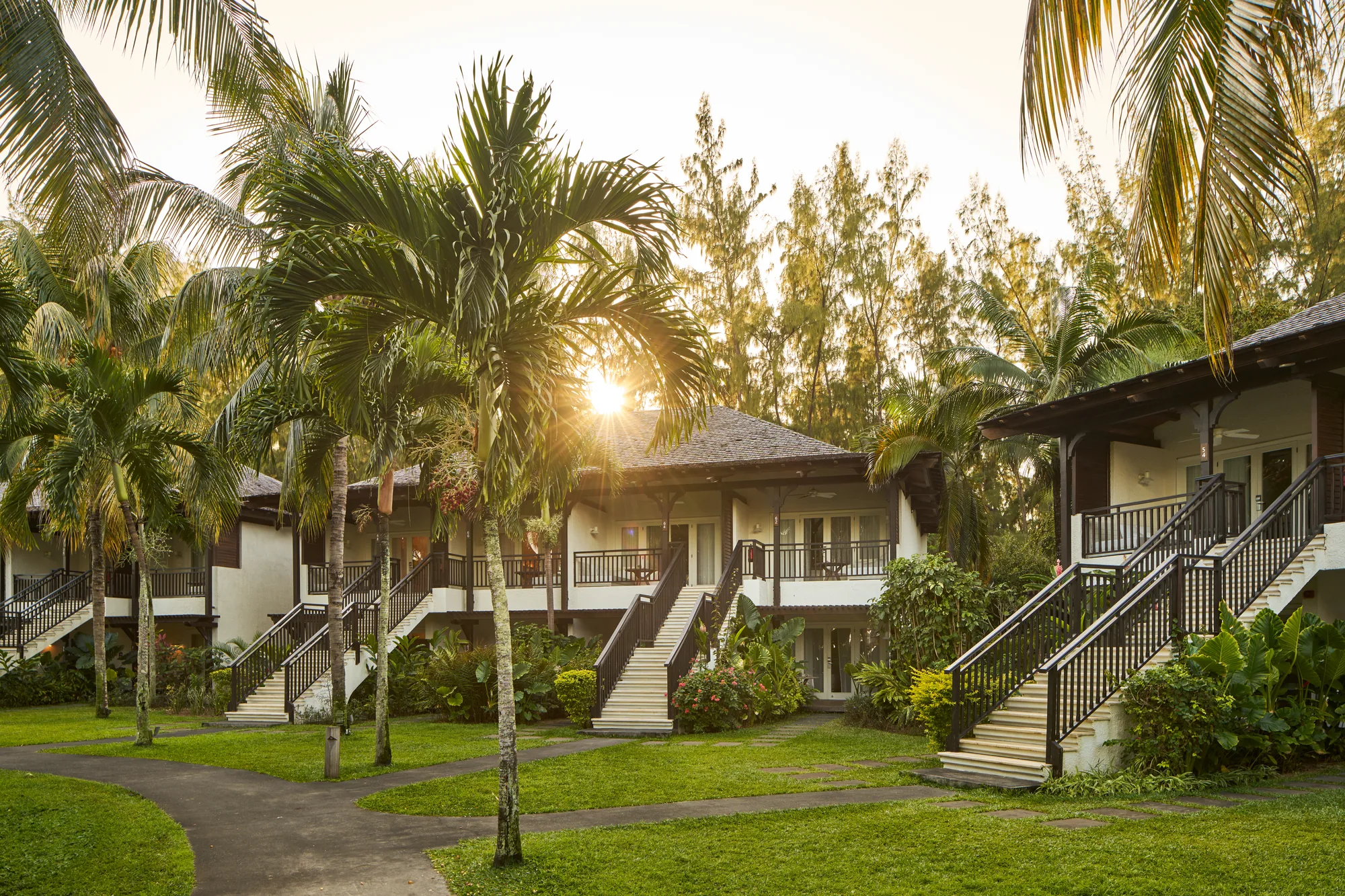 Two-storey accommodation blocks with outside stairs, among palm trees at sunrise