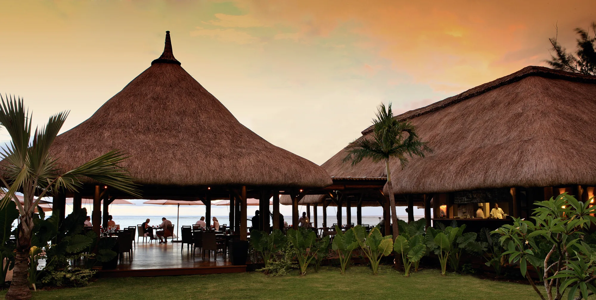 Thatched restaurant pavilions at sunset, with diners on the terrace