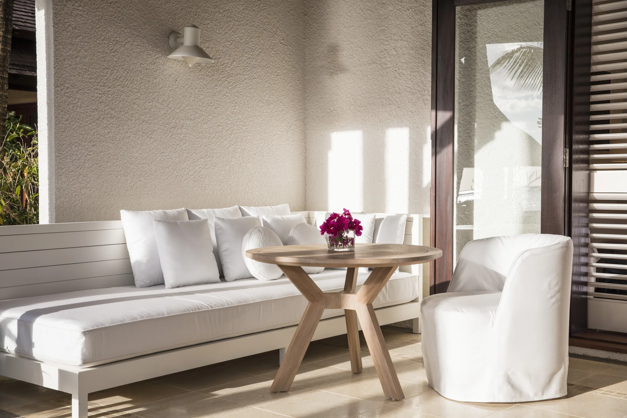 A room with a white sofa, an armchair and a round table beside open shutters