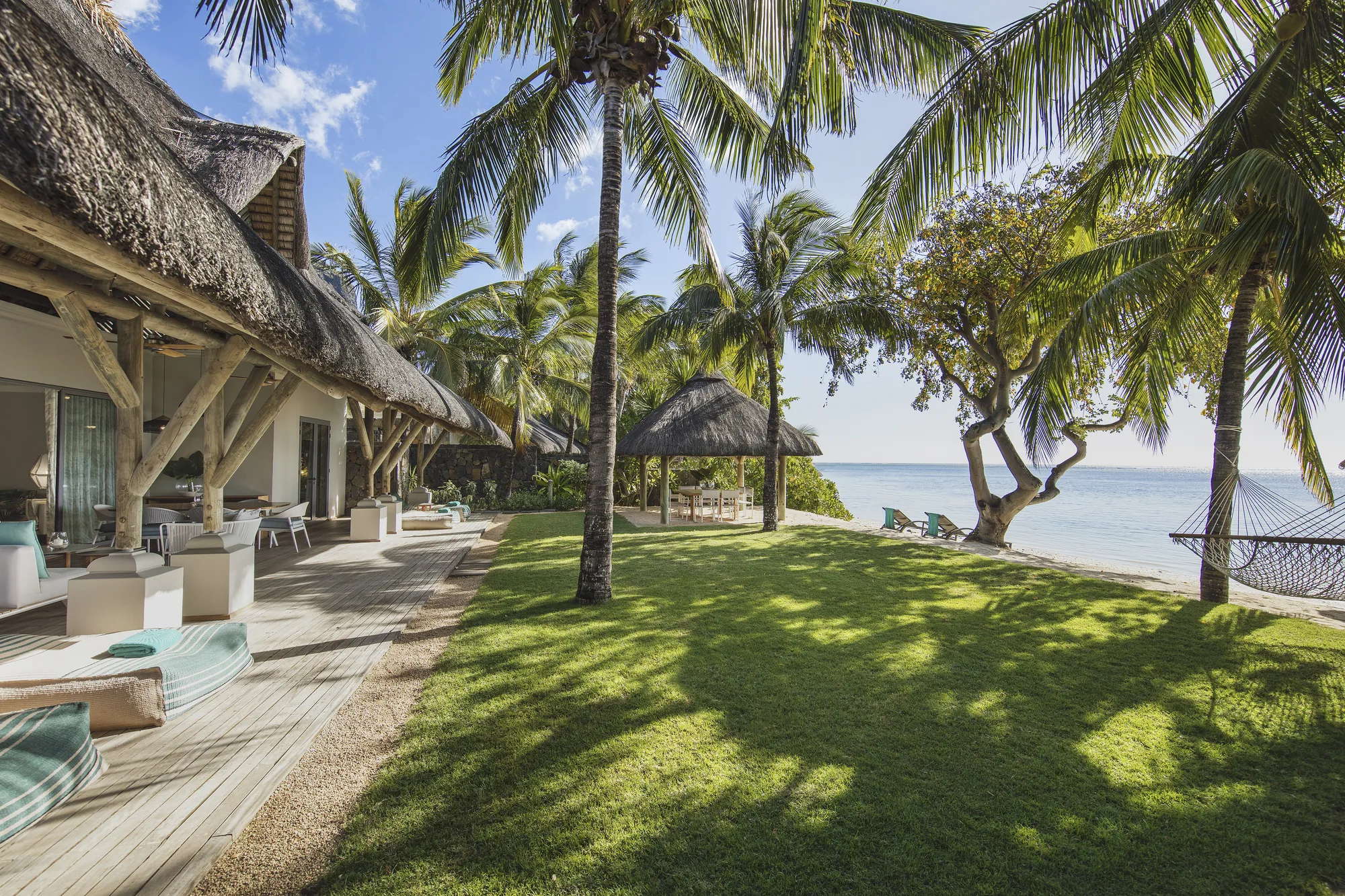 A thatched villa with a lawn, sun loungers and palm trees running down to the sea