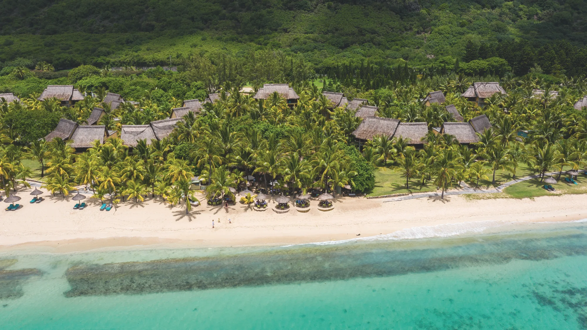 Aerial view of Dinarobin Beachcomber, its thatched roofs in palm groves behind the beach and lagoon