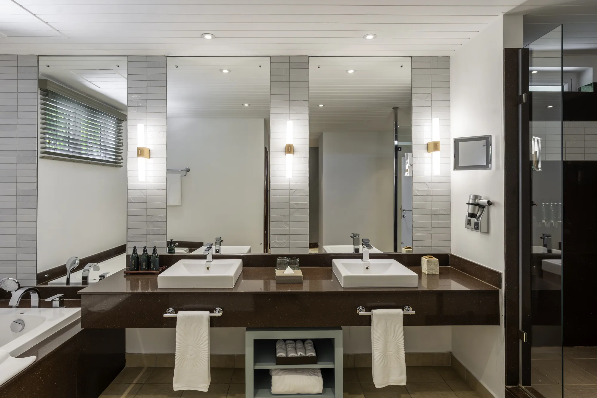 A bathroom with twin basins on a dark vanity under tall mirrors