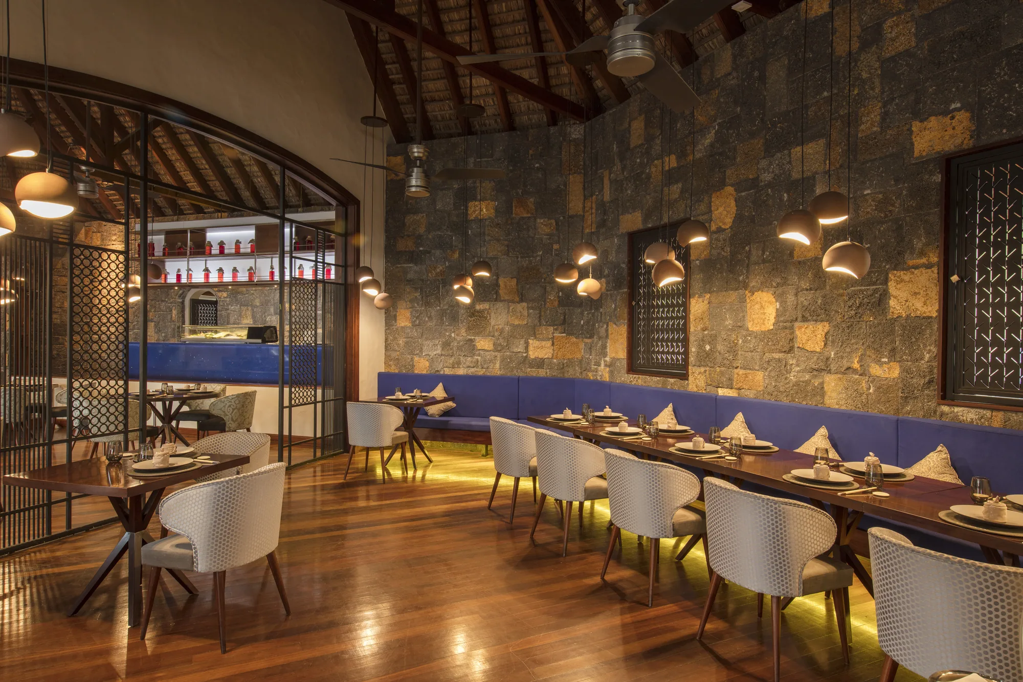 A restaurant with a stone wall, a long banquette and warm pendant lights