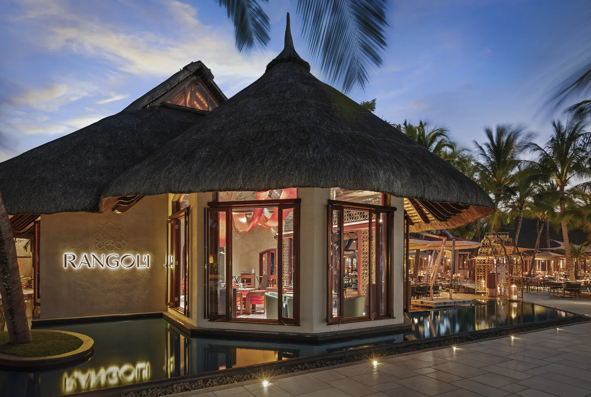 The Rangoli restaurant, a thatched pavilion lit at dusk beside a pool