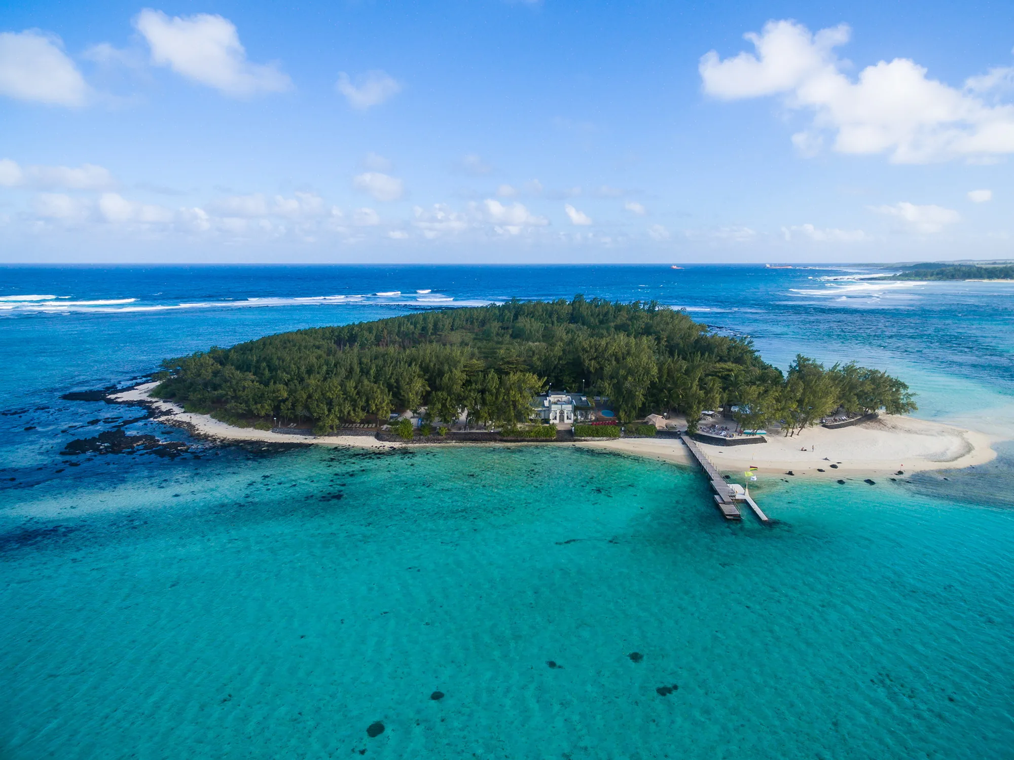 Aerial view of Ile des Deux Cocos, a small wooded island with a jetty in a turquoise lagoon