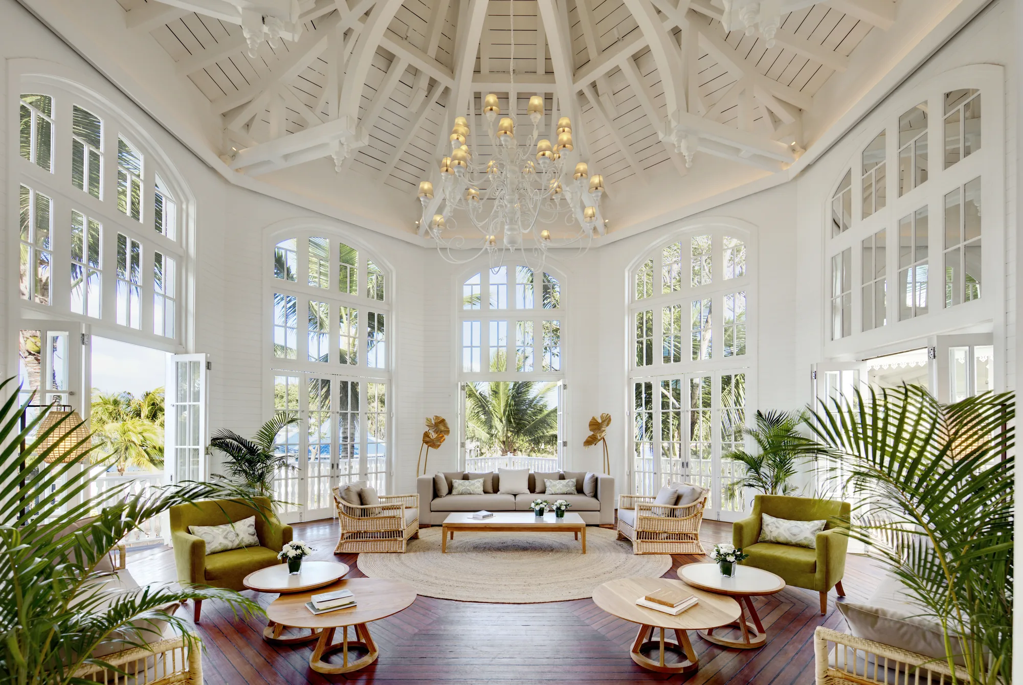 A white drawing room with a high timbered ceiling, a chandelier and tall windows