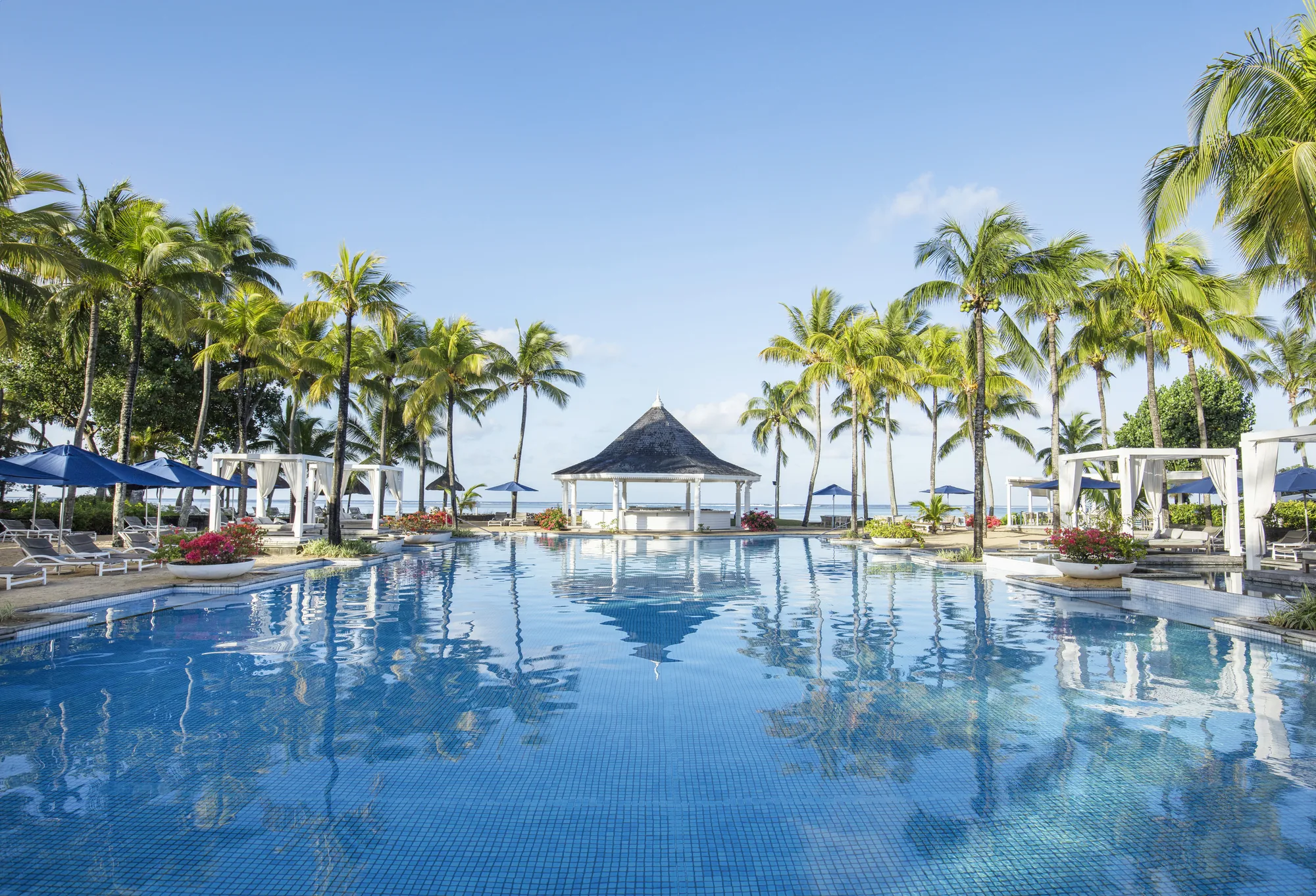 The pool at Heritage Le Telfair Golf & Wellness Resort, lined with palms and a pavilion by the sea