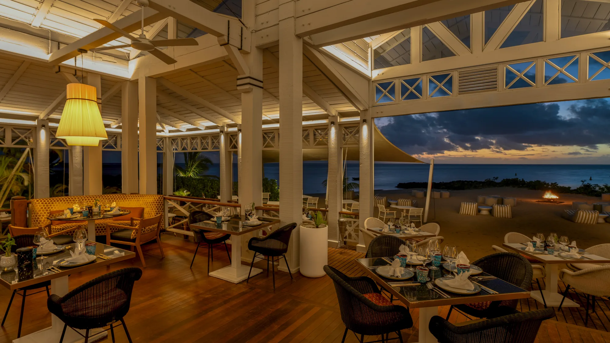 A restaurant terrace at dusk, with tables set and the sea beyond