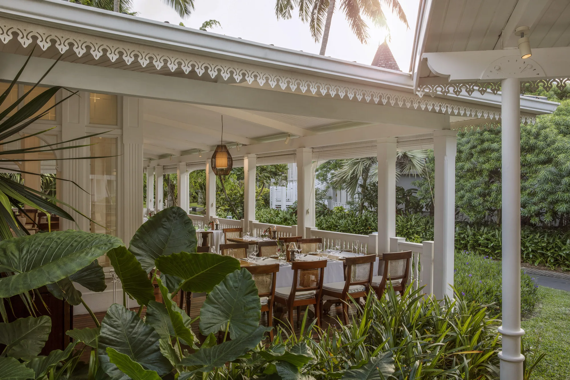 A veranda restaurant with laid tables, framed by garden planting