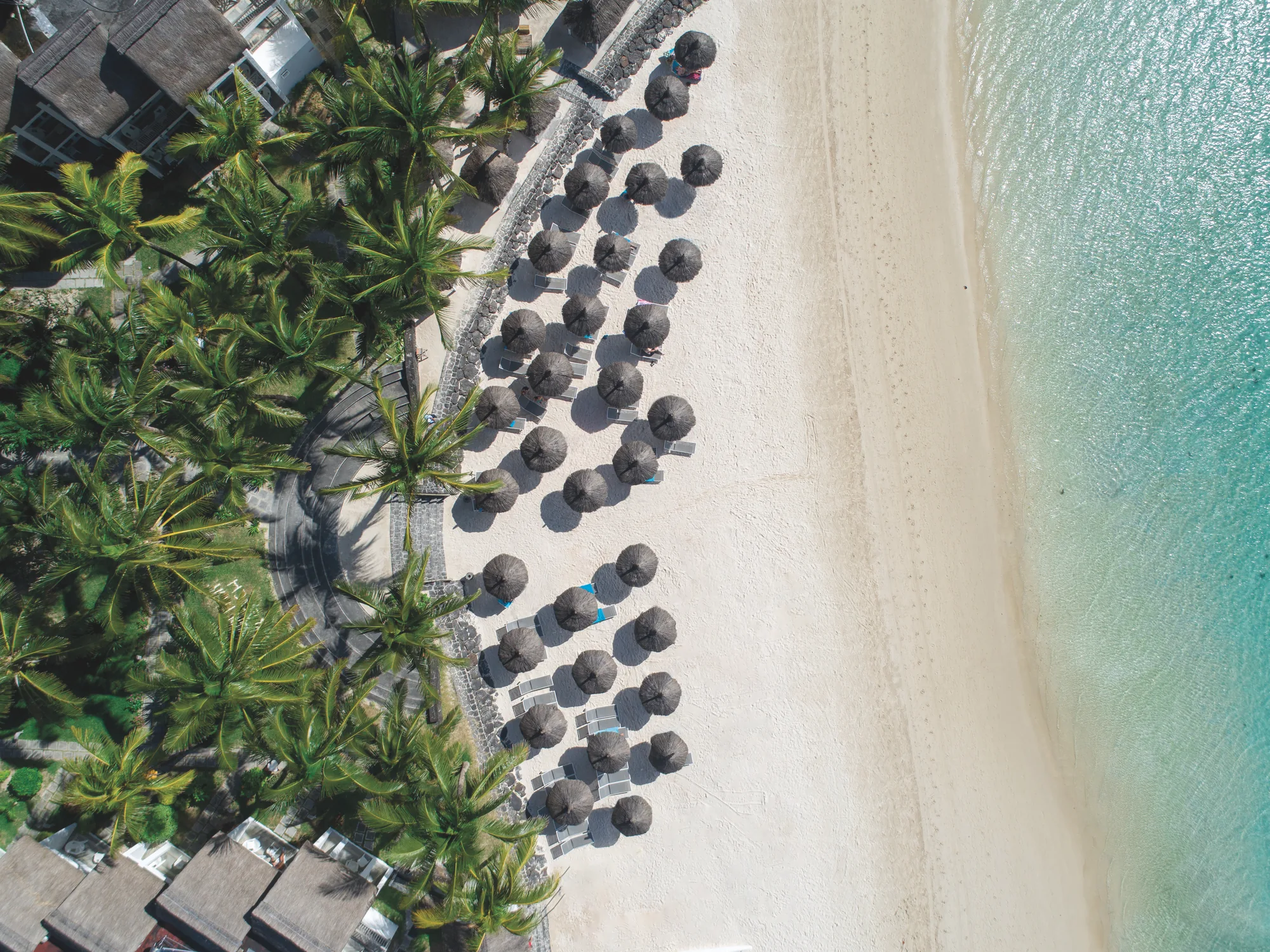 Aerial view of Veranda Belle Mare, rows of parasols along the beach beside a turquoise lagoon