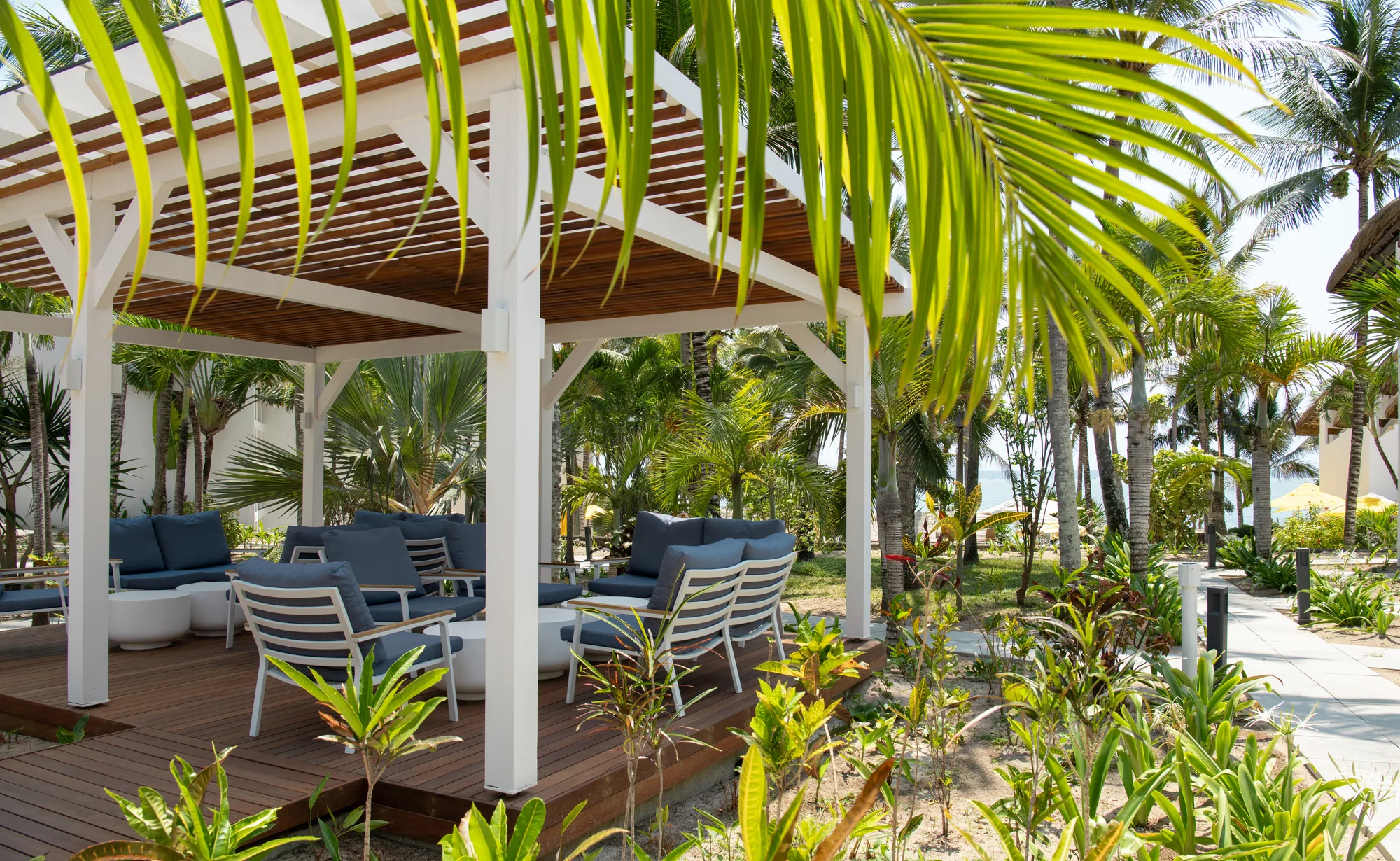 A pergola with blue outdoor sofas among palm fronds