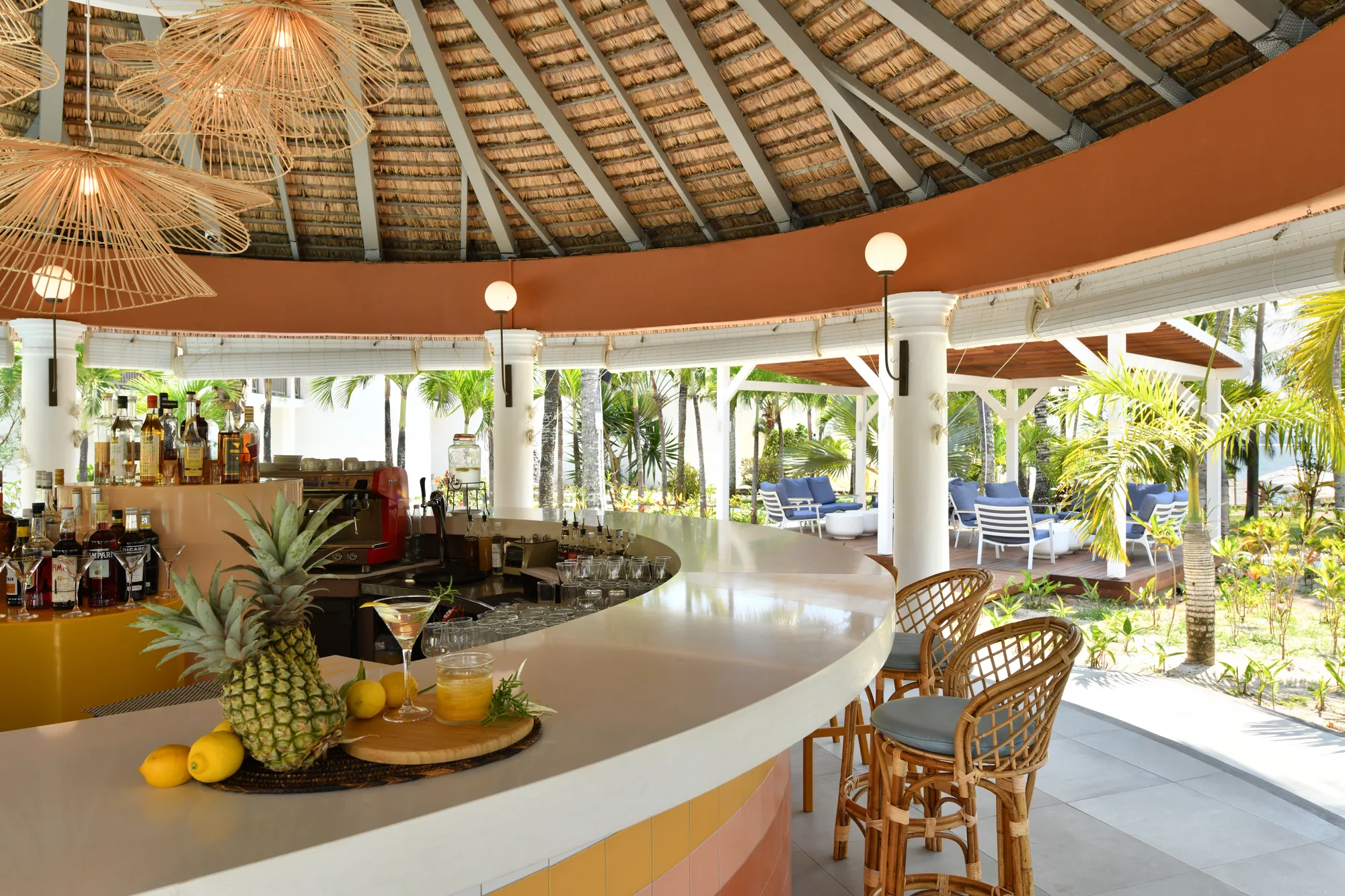 A curved bar counter with a pineapple and drinks, open to the garden