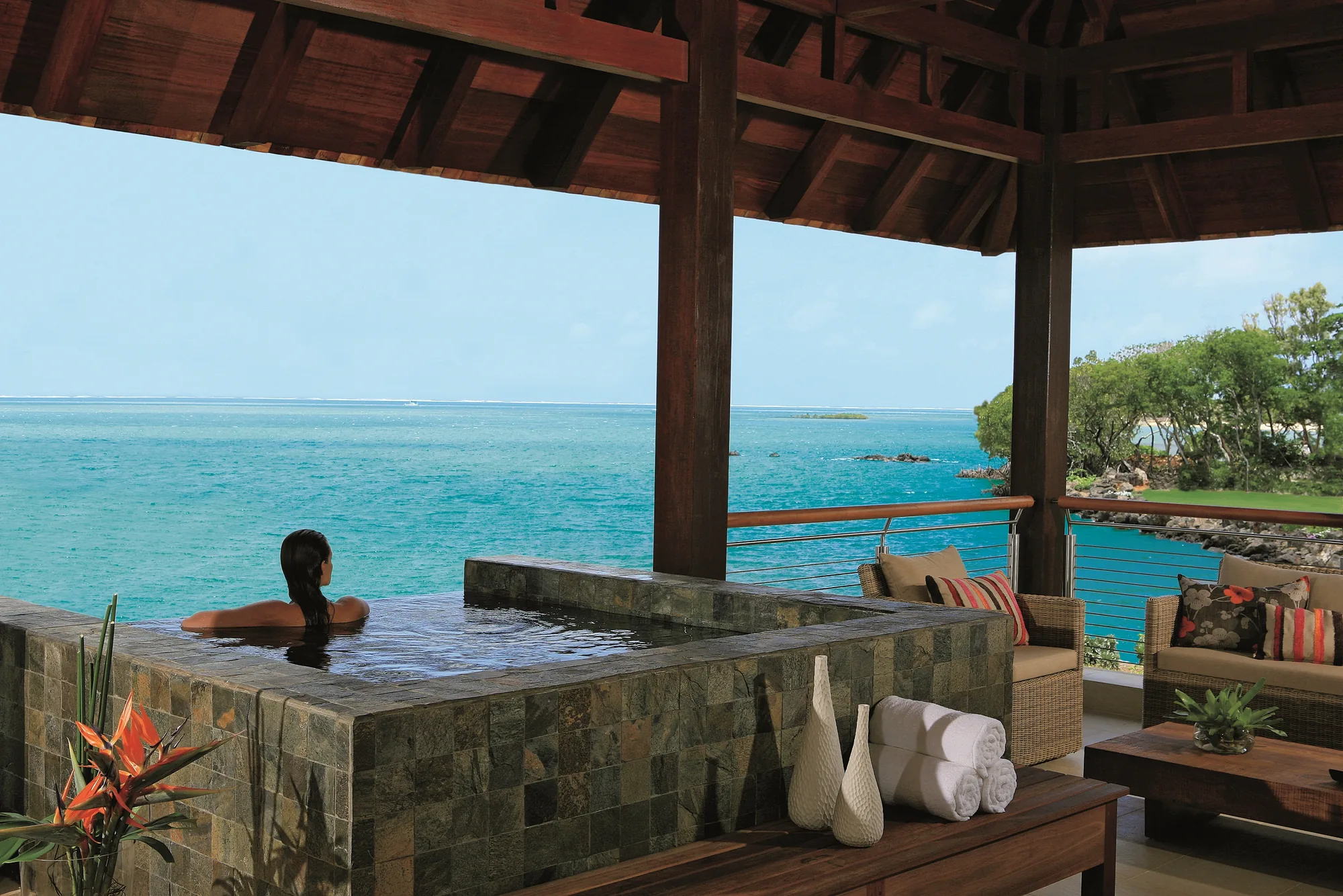 A guest in a plunge pool on a covered terrace overlooking the sea