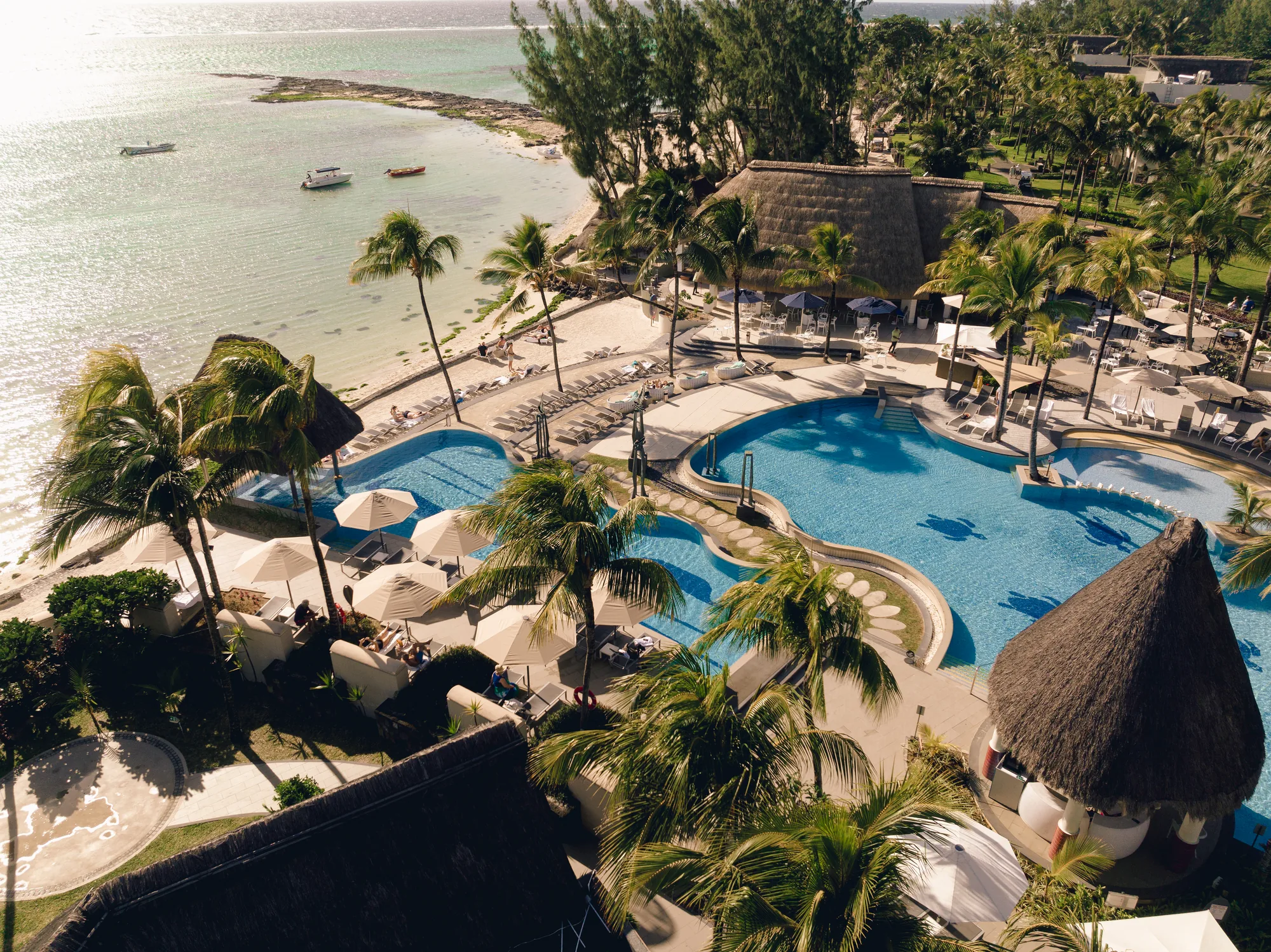 Aerial view of Ambre, A Sunlife Resort, its pools and thatched roofs beside the beach and lagoon