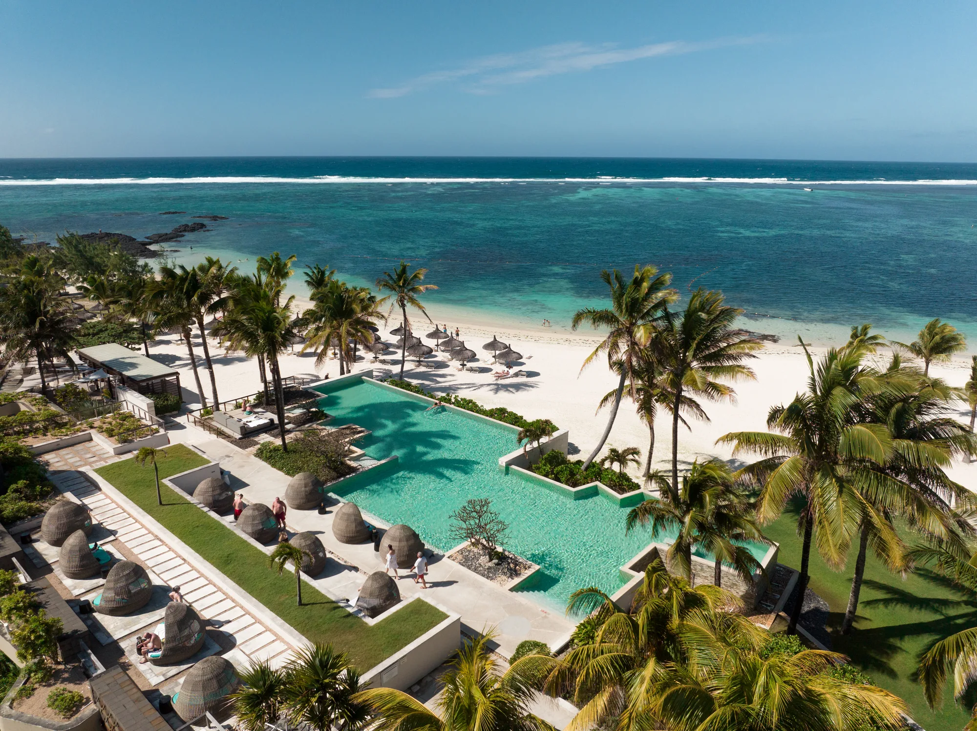 Aerial view of Long Beach, A Sunlife Resort, its long pool and parasols beside the beach and reef