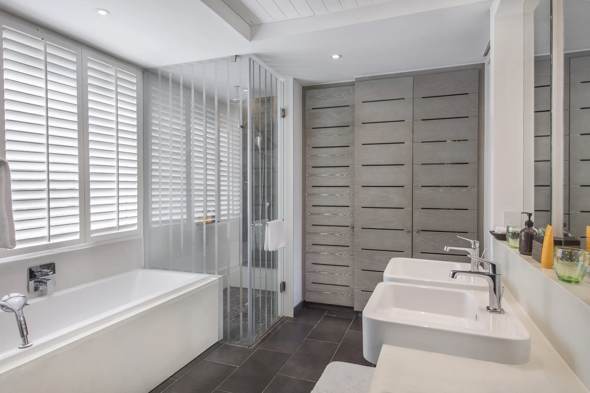 A bathroom with a bath, twin basins and shuttered windows