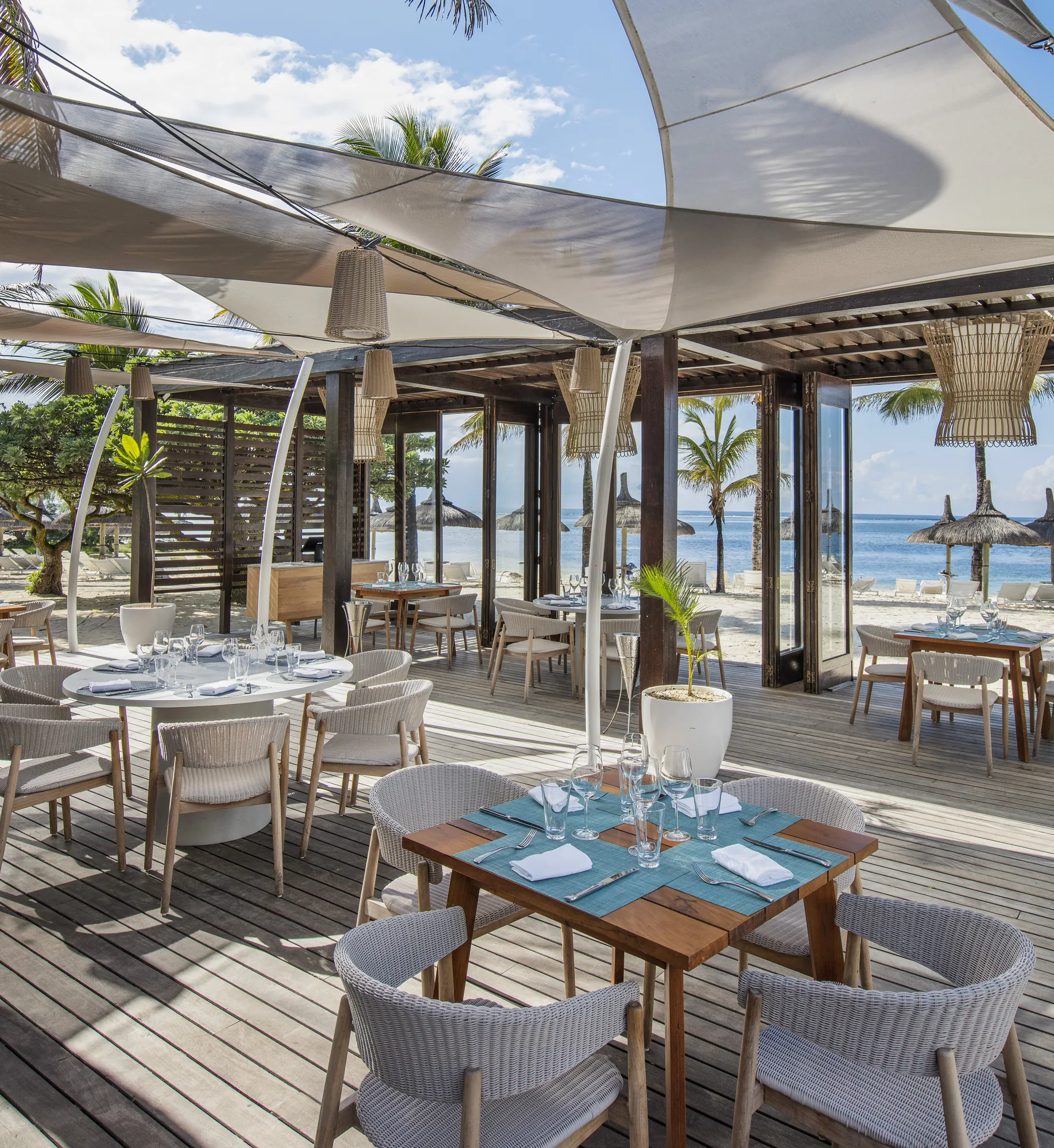 A beachfront restaurant terrace with tables under shade sails
