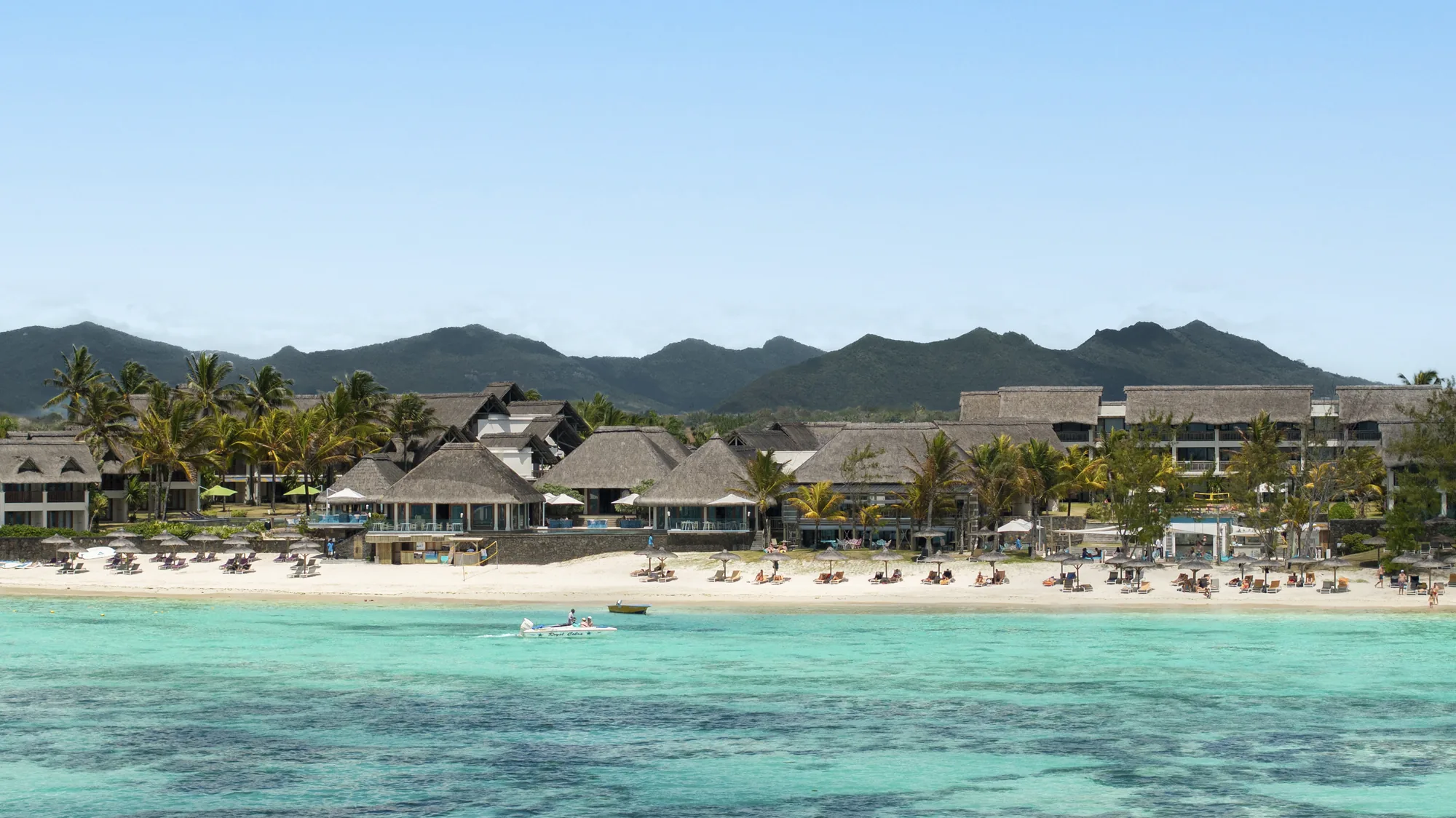 C Mauritius on the Palmar shore, its thatched buildings behind the beach and lagoon with hills beyond