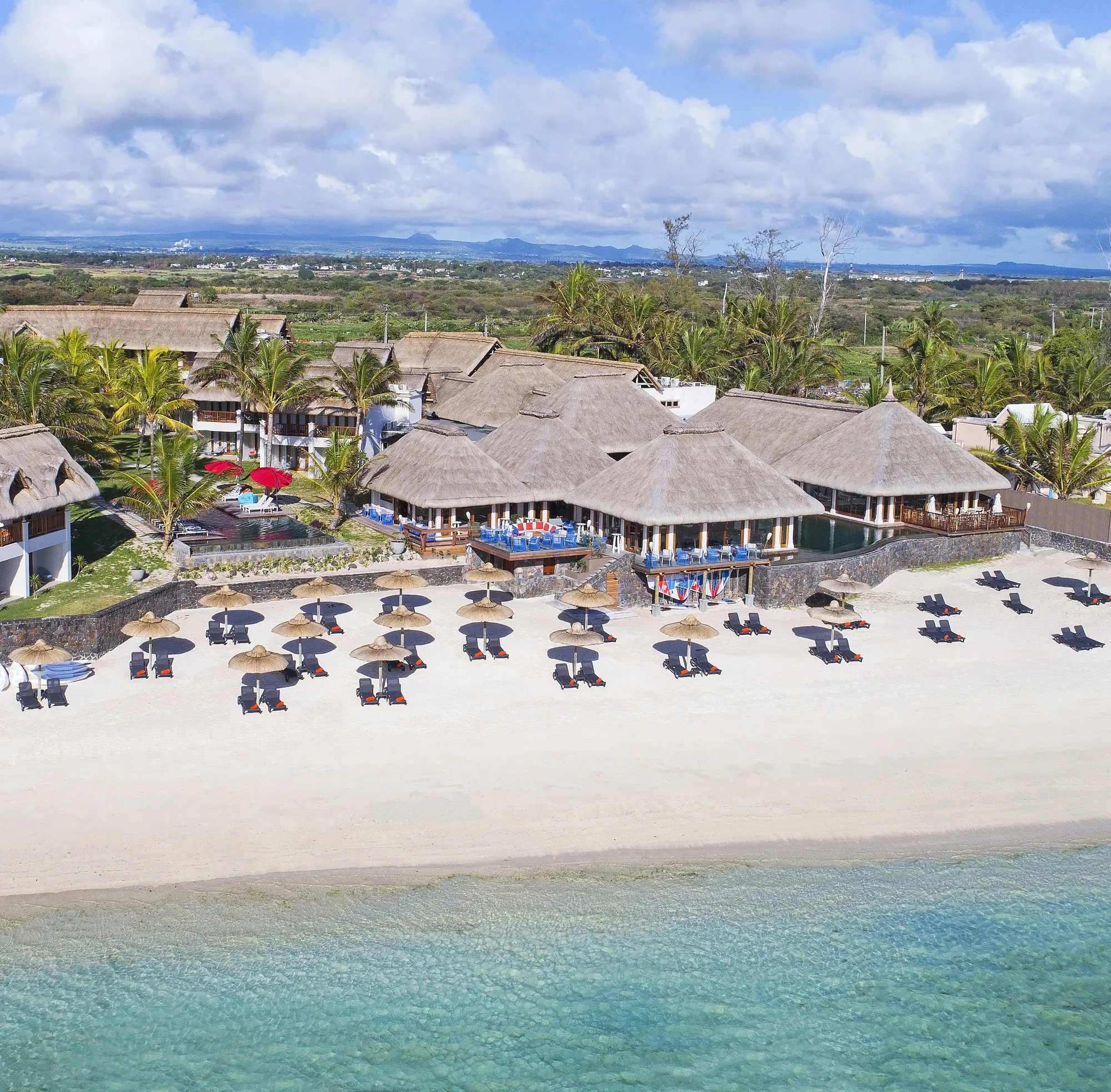 Aerial view of the beach with rows of parasols in front of the thatched resort buildings