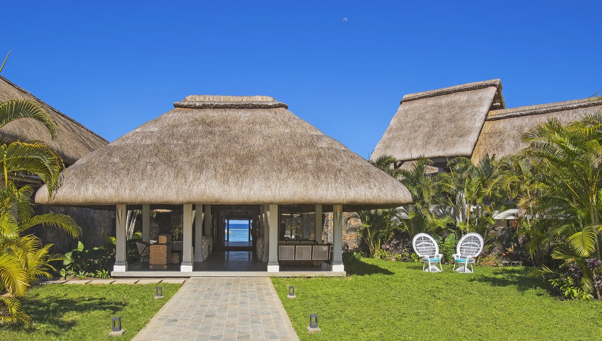 A thatched pavilion at the end of a garden path, open towards the sea